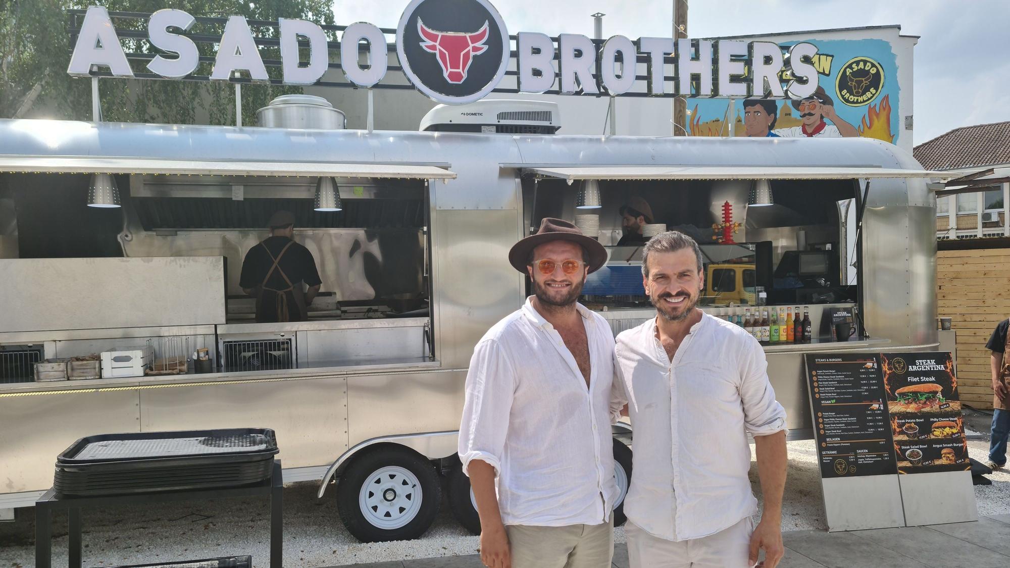 Zwei Männer in weißen Leinenhemden stehen vor einem silbernen Foodtruck.