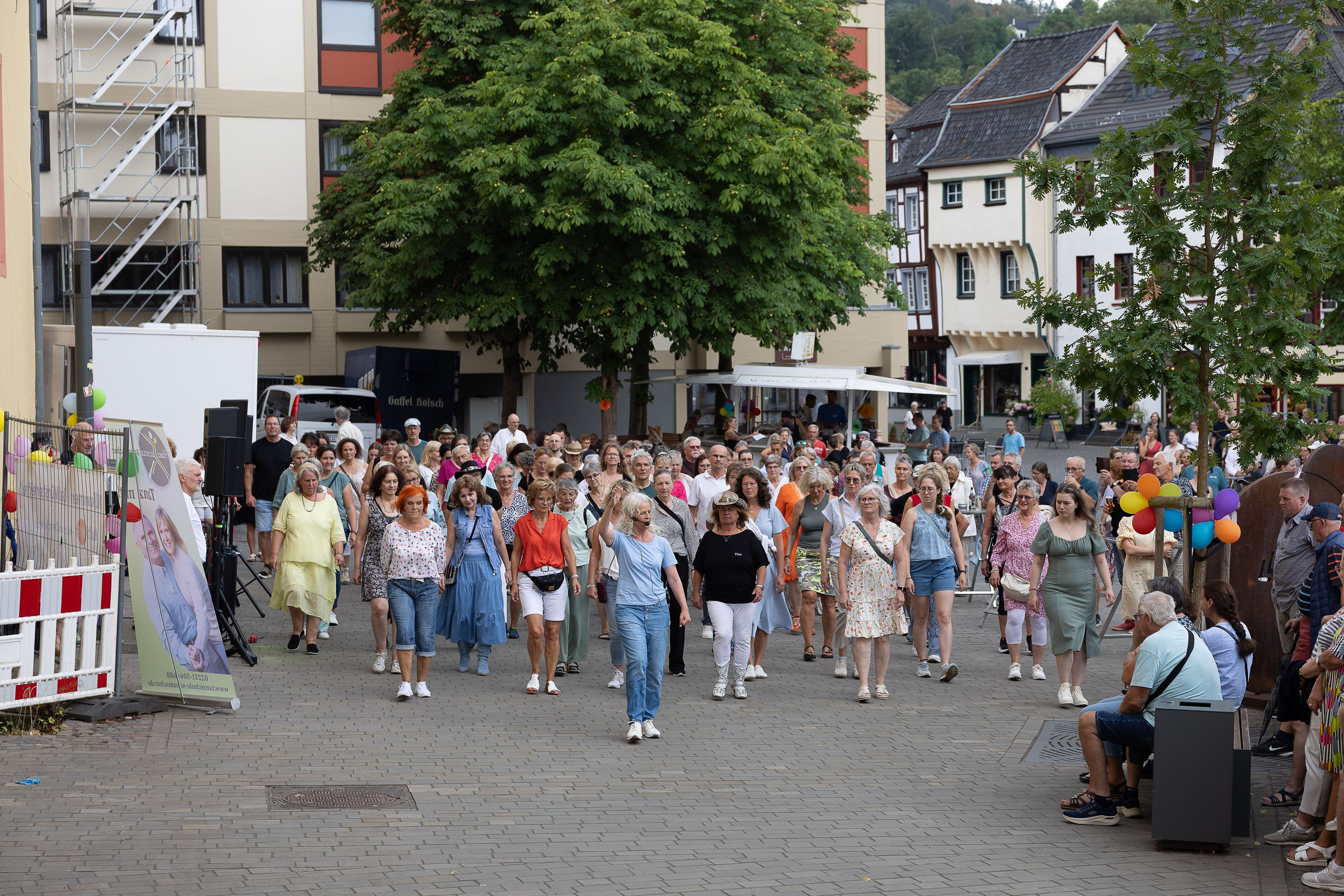 Viele Tanzbegeisterte, vornehmlich Frauen, stehen hinter der Tanzlehrerin, die ihren rechten Arm erhoben hat.