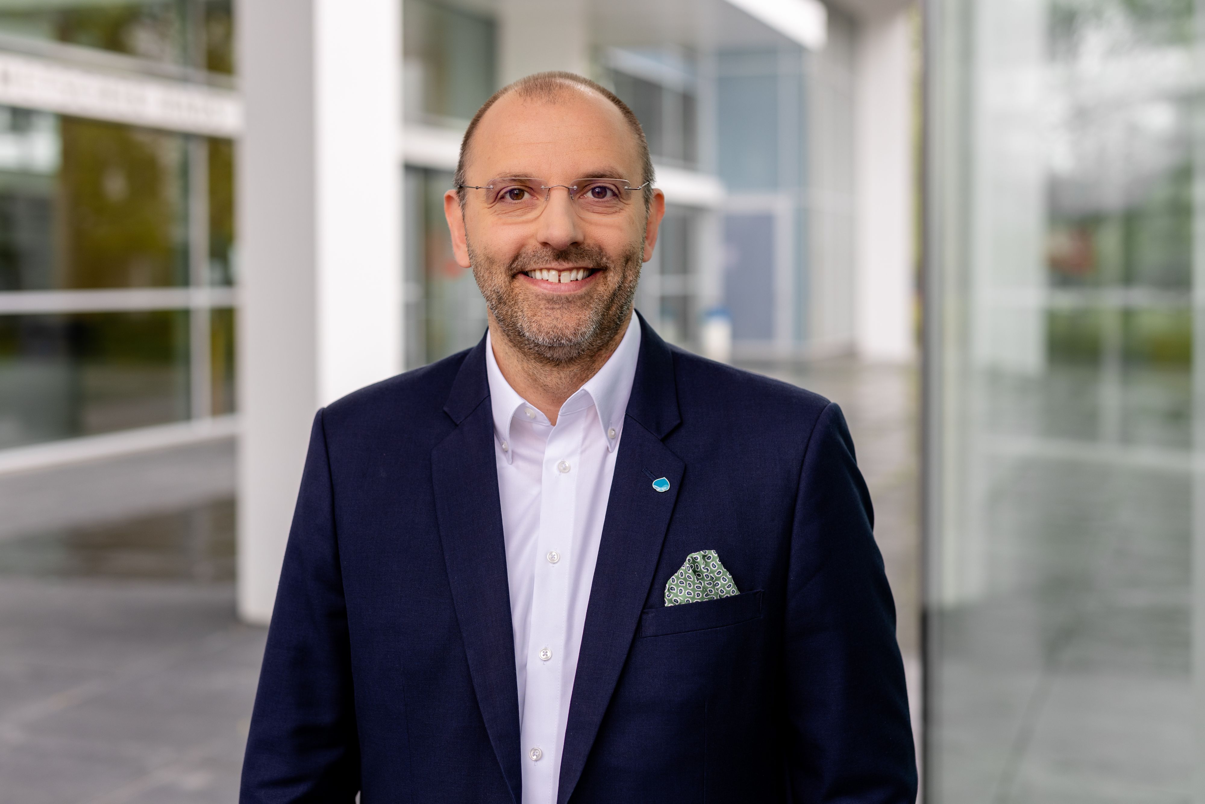 Peter Fintl trägt einen blauen Anzug und blickt lächelnd in die Kamera.