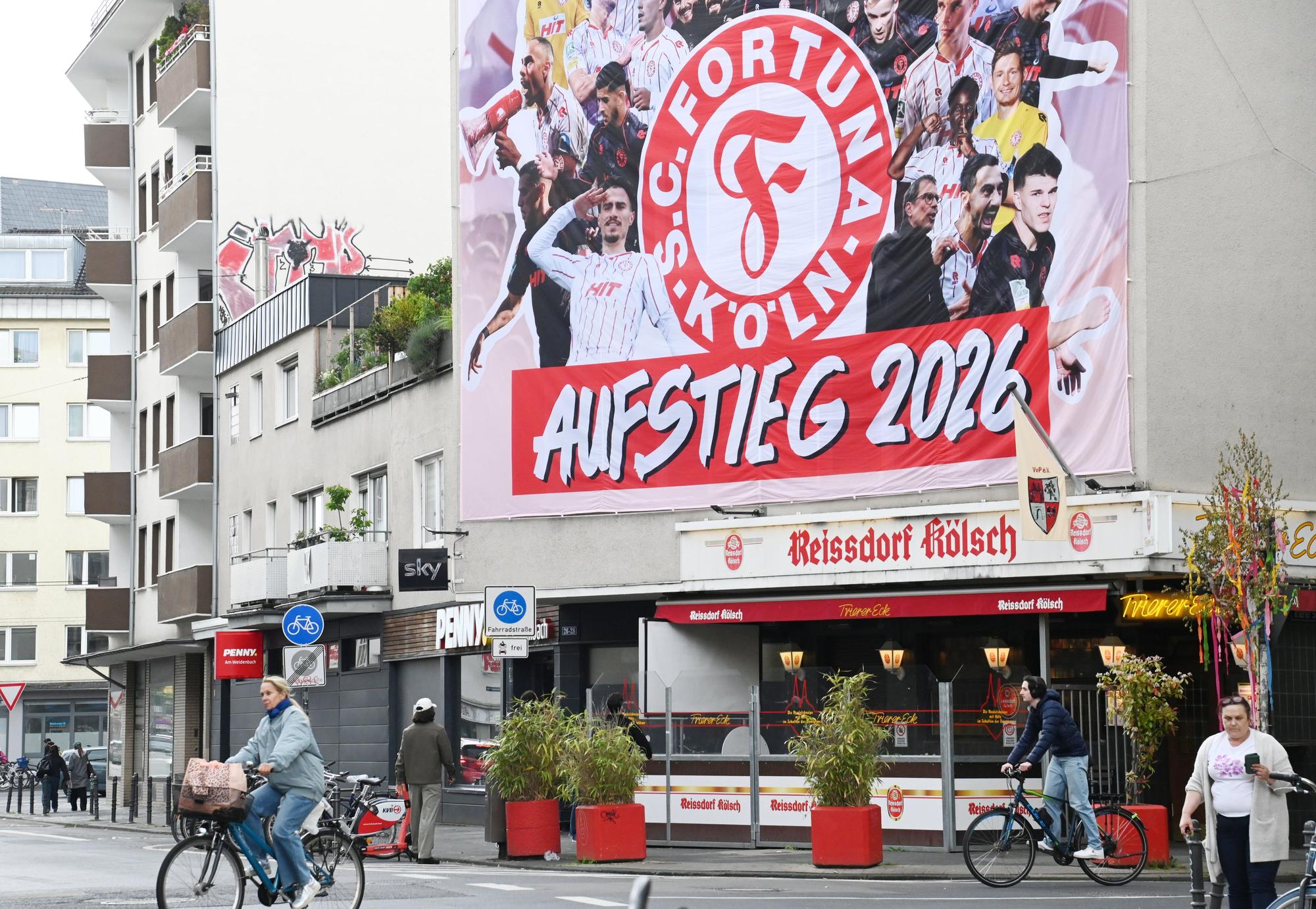 An einer Hauswand hängt ein Transparent zum Aufstieg von Fortuna Köln in die Dritte Liga.