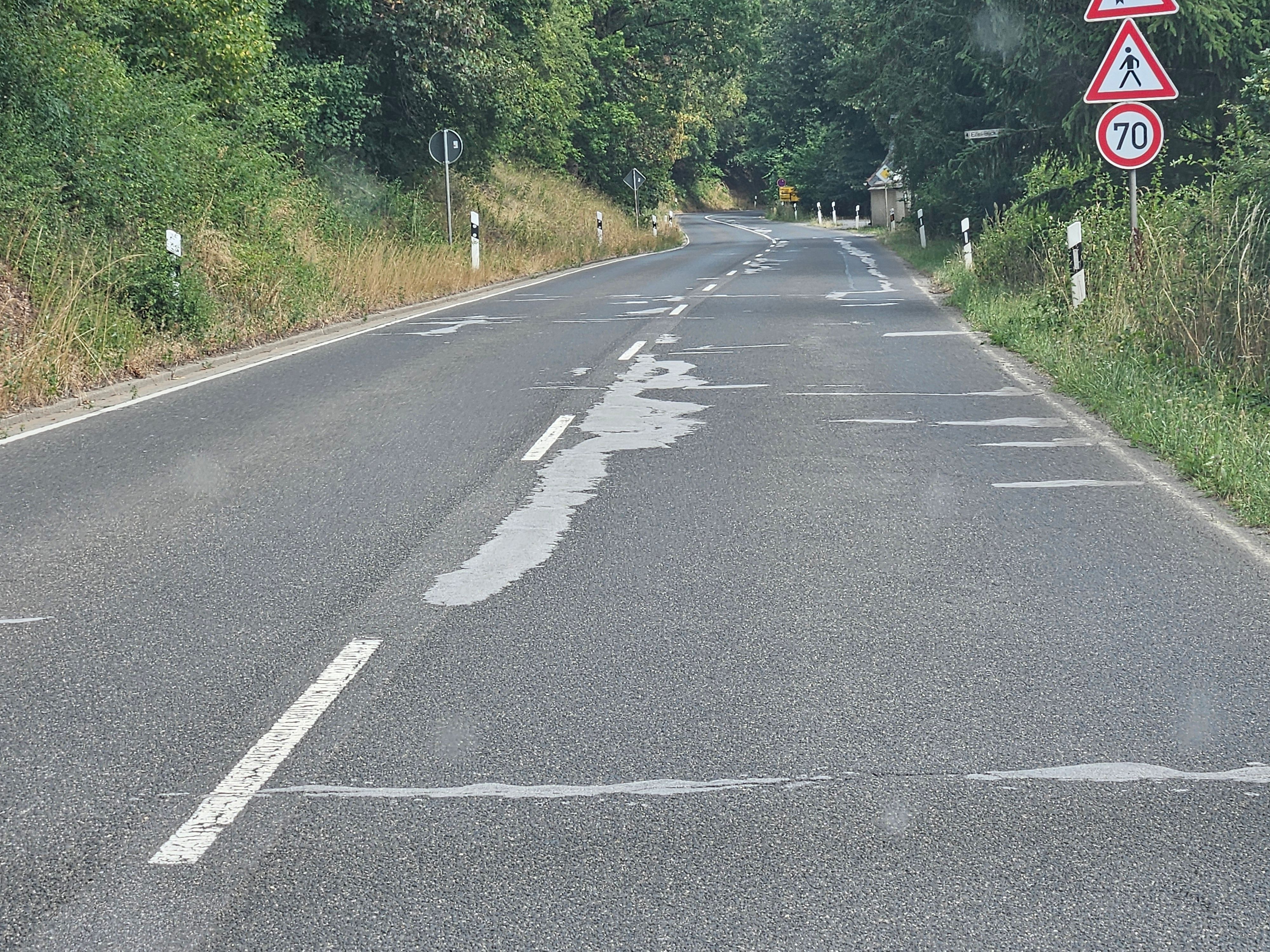 Zu sehen ist eine Straße mit mehreren hellen Ausbesserungsstellen.