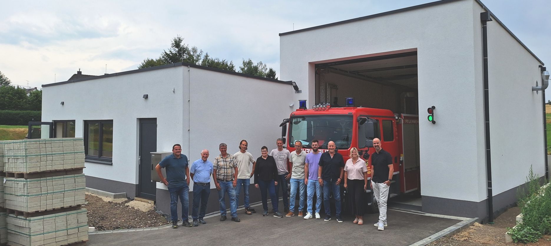 Die Genannten haben sich zum Gruppenbild vor der Wagenhalle mit dem Löschfahrzeug und dem Gerätehaus aufgestellt.