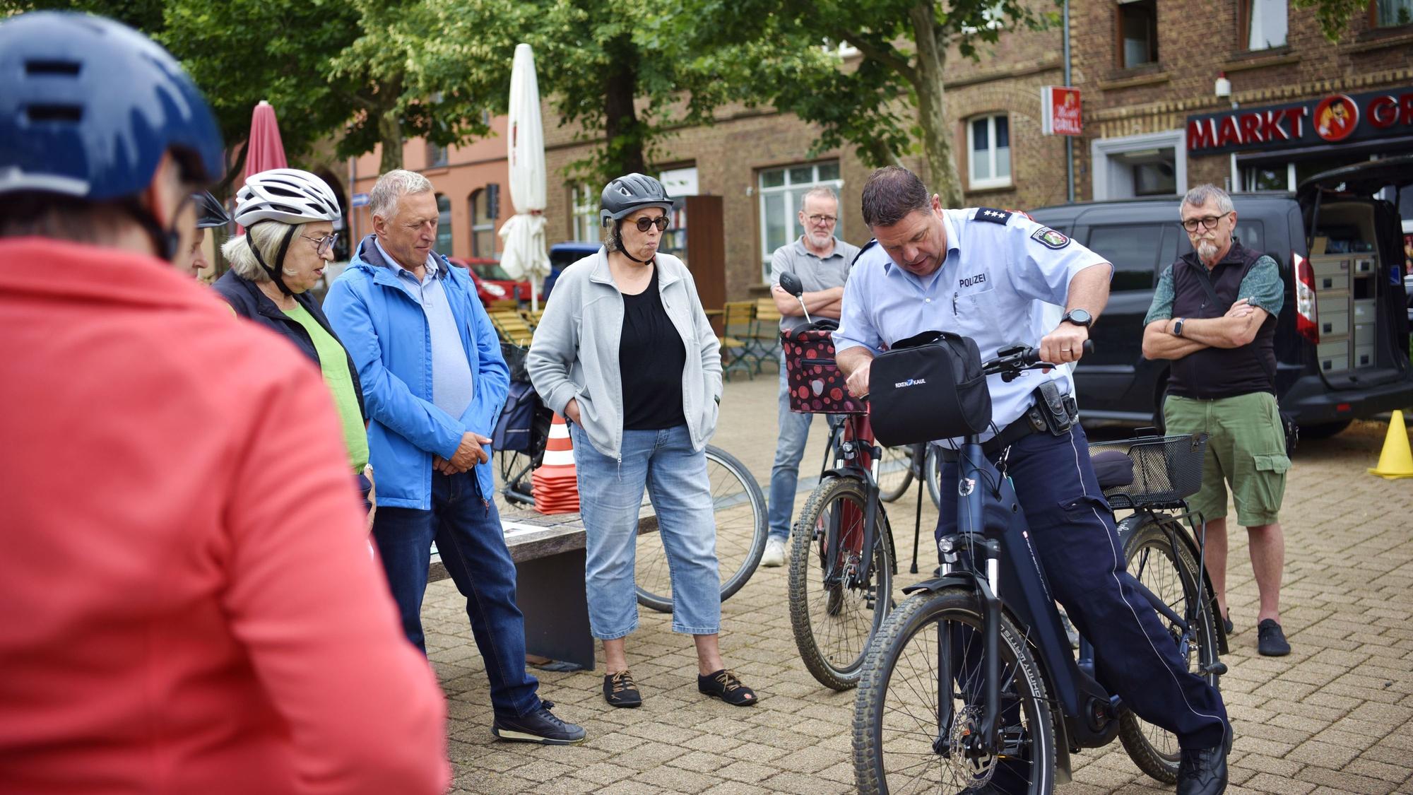 Ein Polizist steigt umringt von Menschen mit Fahrradhelmen auf ein Pedelc.
