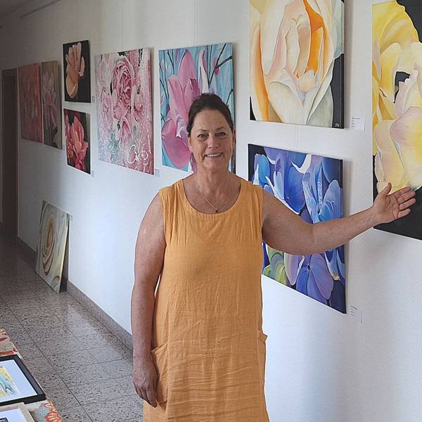 Eine Frau in eine gelben Kleid zeigt auf Bilder einer Ausstellung, die Blüten zeigen.
