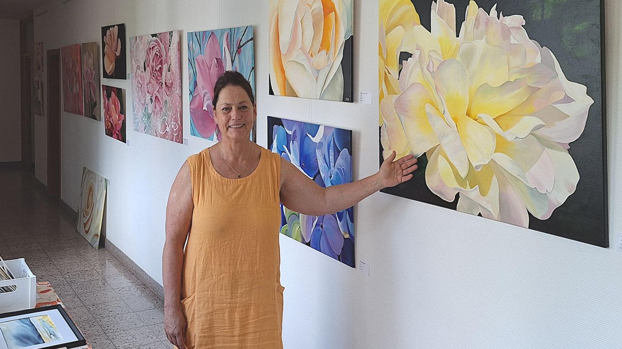 Eine Frau in eine gelben Kleid zeigt auf Bilder einer Ausstellung, die Blüten zeigen.
