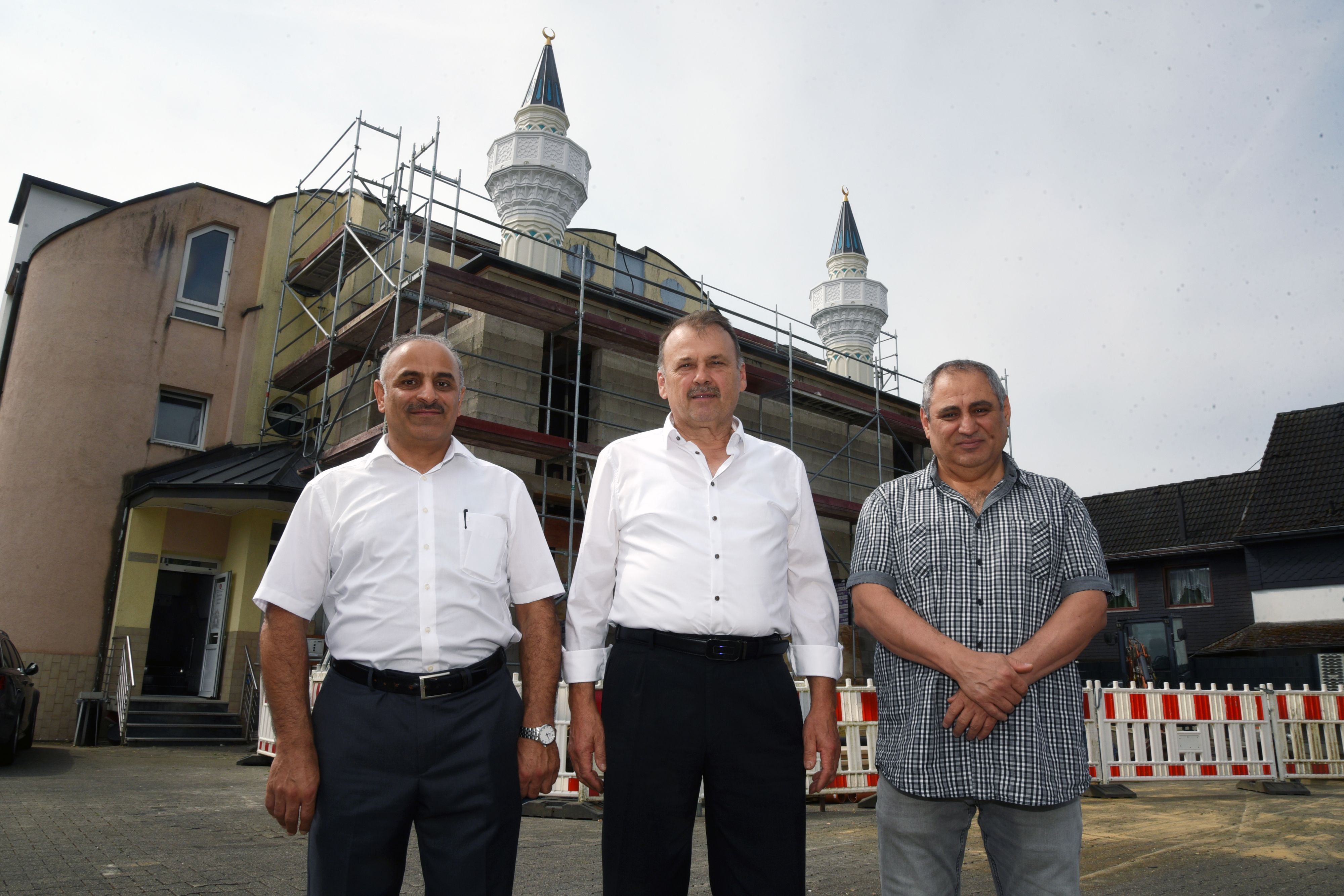 Drei Männer stehen vor einer Moschee, die sich gerade im Umbau befindet.