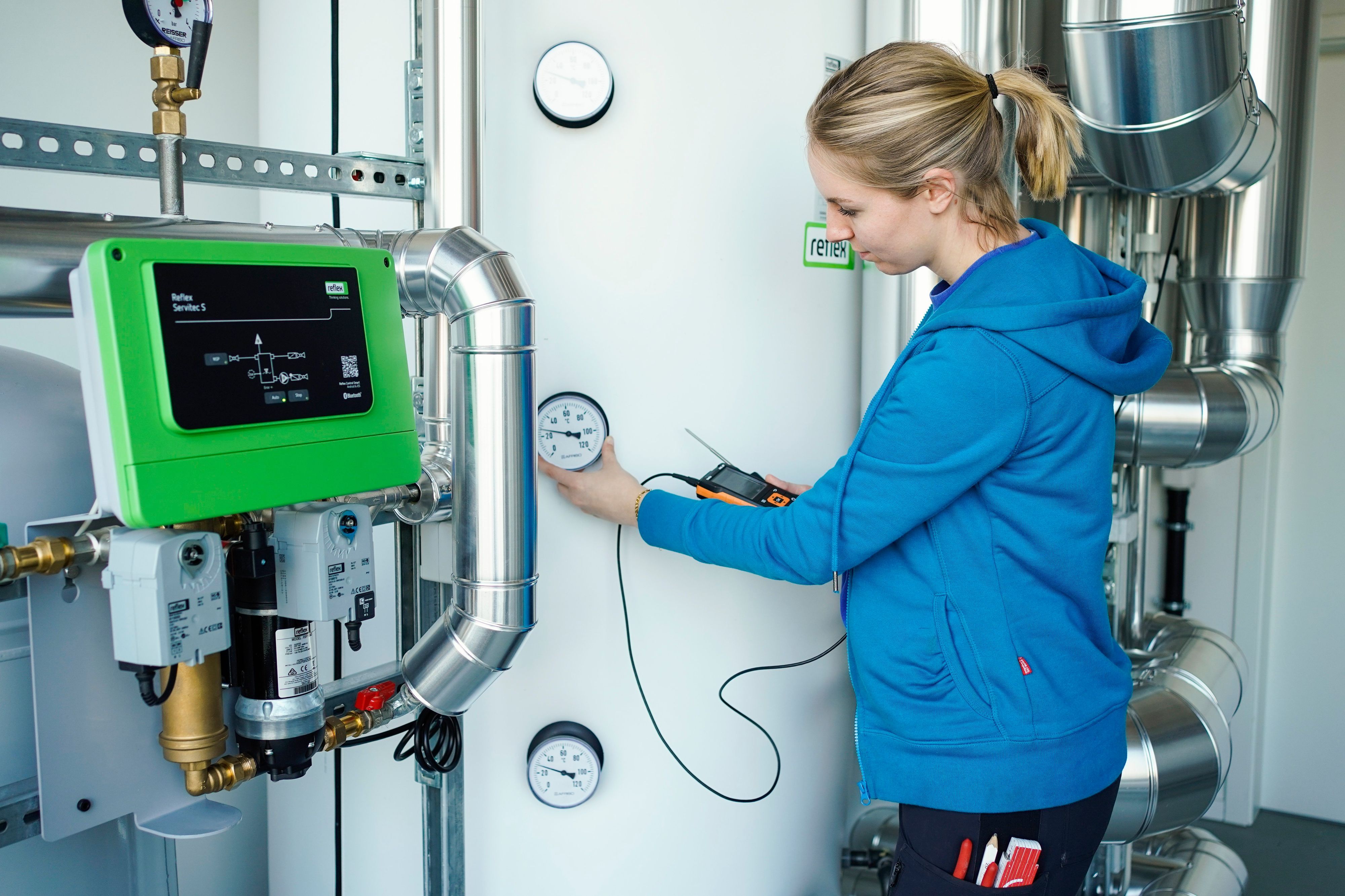 Eine junge Frau in blauer Sweatshirt-Jacke hält ein Elektronisches Messgerät n der Hand und begutachtet eine Temperaturanzeige.