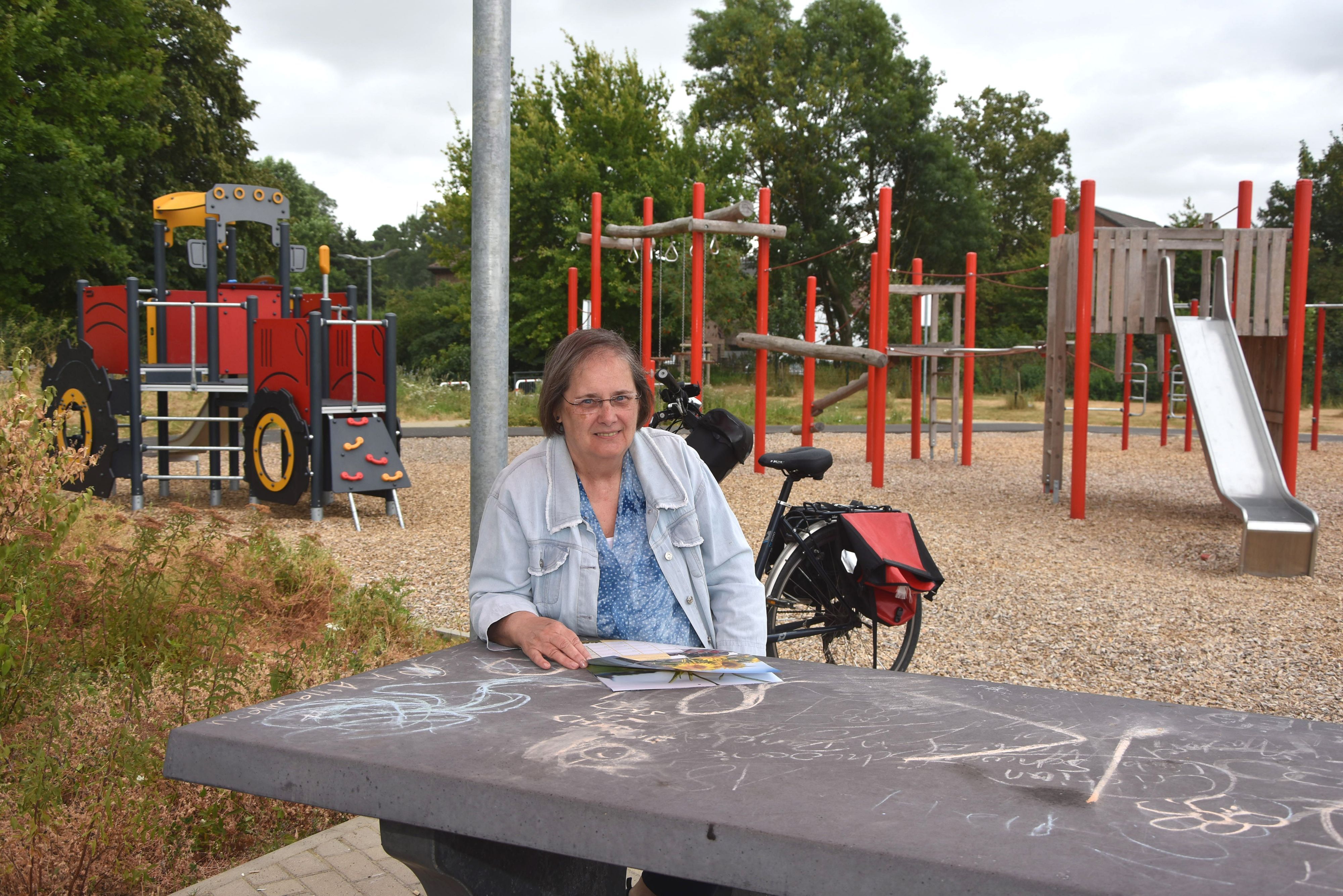 Das Foto zeigt eine Frau, die an einem Tisch vor einem Spielplatz sitzt.