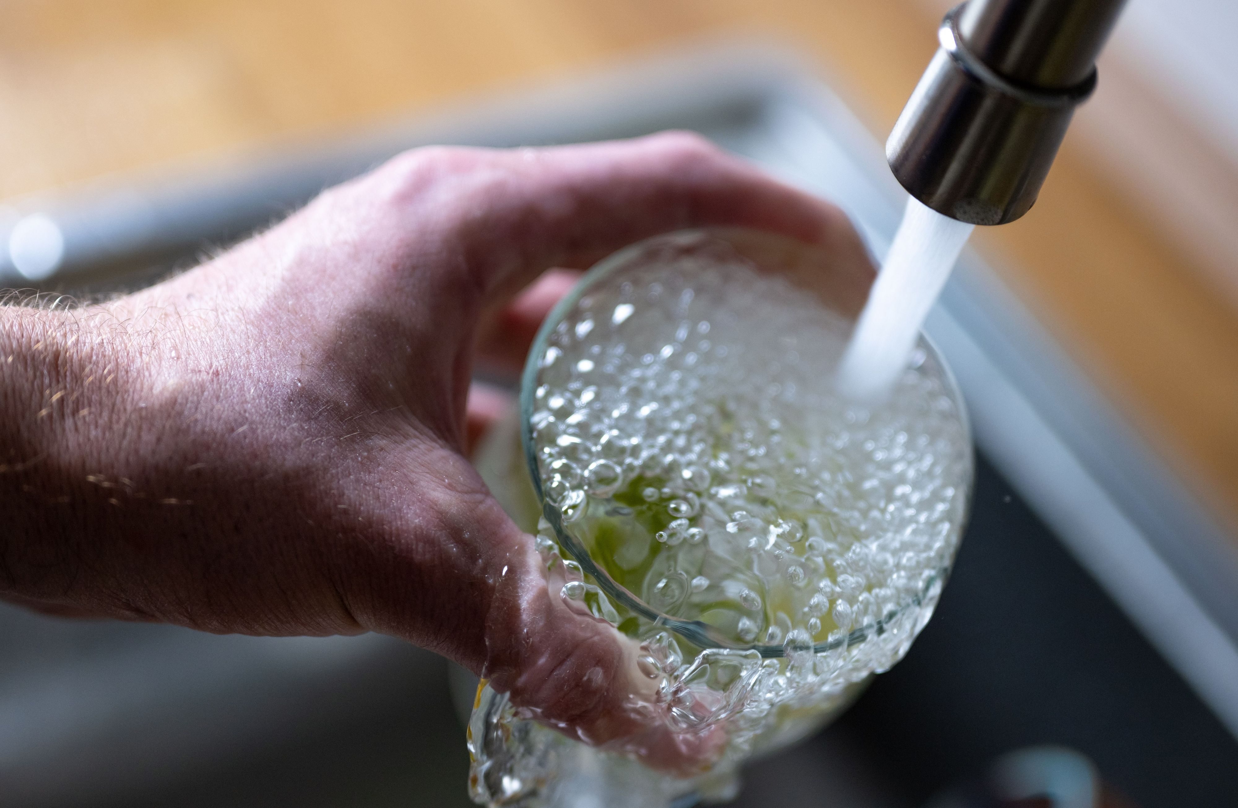 Tinkwasser läuft aus dem Wasserhahn in einer Küche in ein Glas mit Limettenstücken.