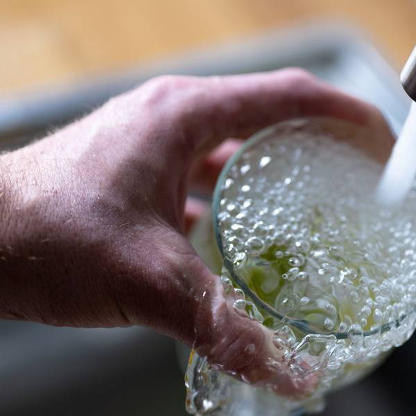 Tinkwasser läuft aus dem Wasserhahn in einer Küche in ein Glas mit Limettenstücken.