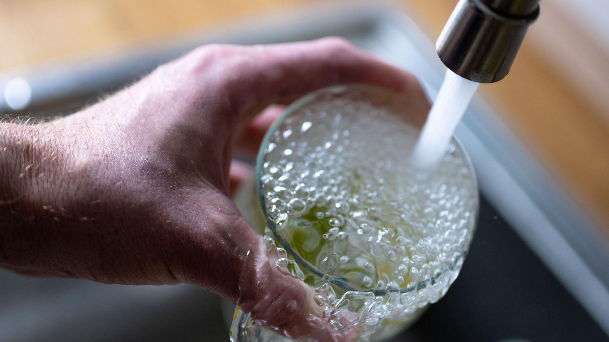Tinkwasser läuft aus dem Wasserhahn in einer Küche in ein Glas mit Limettenstücken.