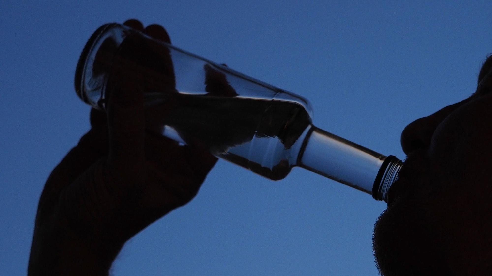 Ein Mann trinkt am Abend aus einer kleinen Flasche Schnaps.