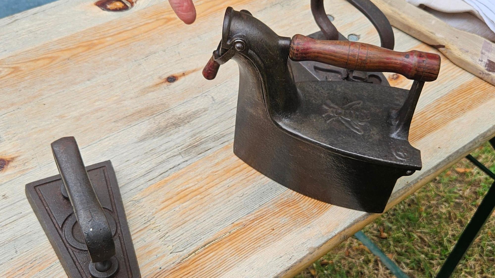 Zwei historische Bügeleisen aus Metall stehen auf einem Biertisch.