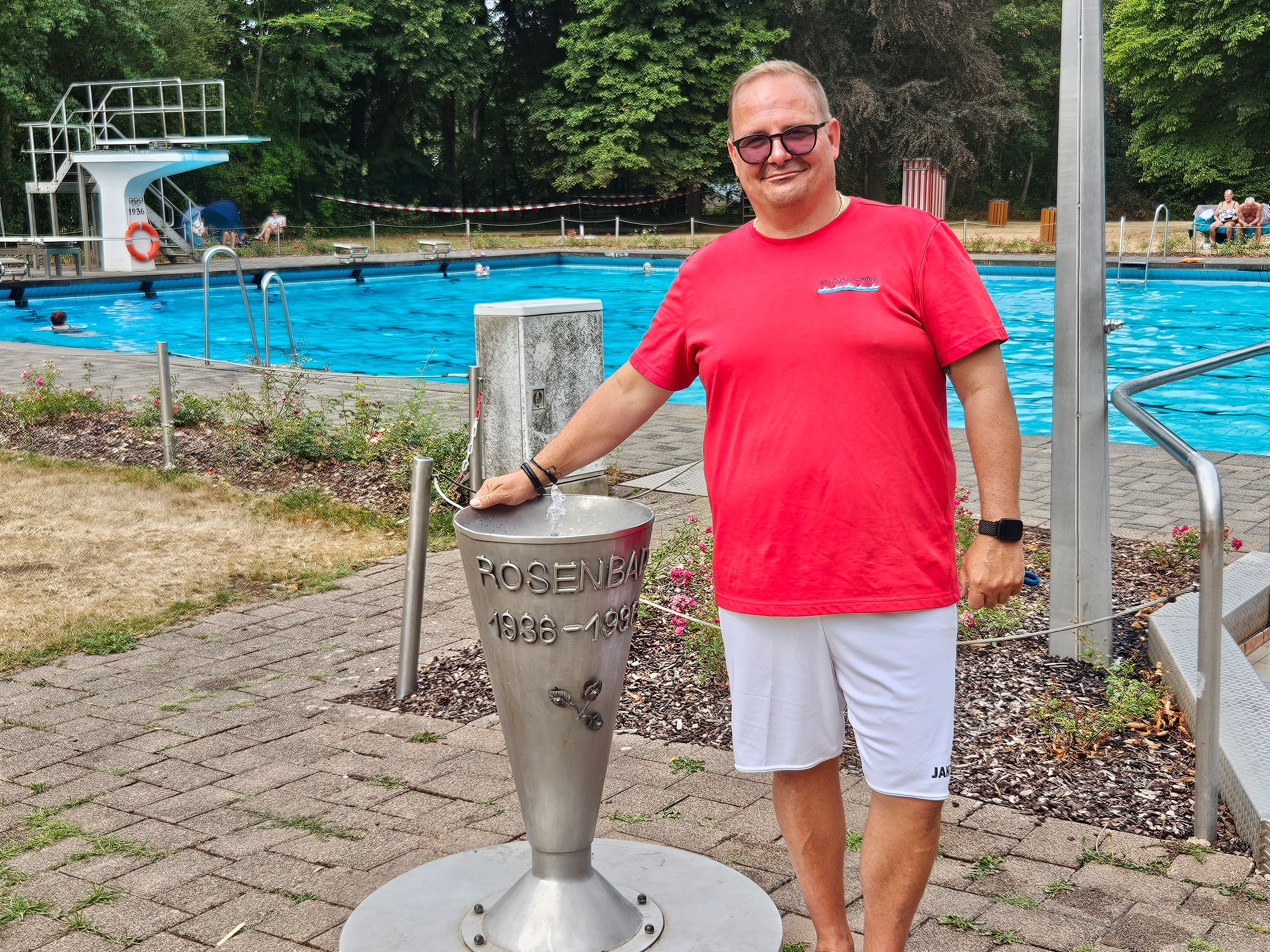 Der Badleiter mit einem roten T-Shirt und einer weißen kurzen Hose steht an einem Wasserspeier im Schwimmbad.