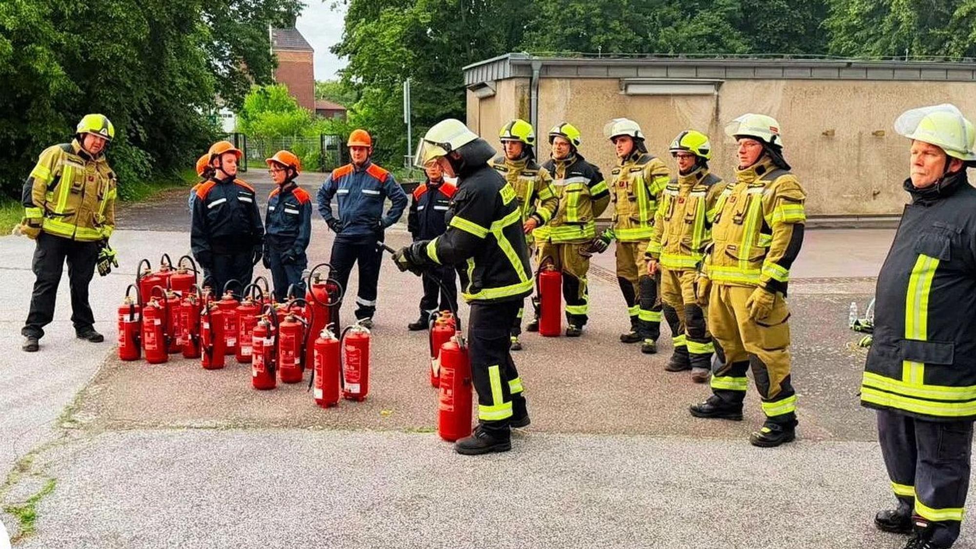 Feuerwehrleute und Mitglieder der Jugendfeuerwehr stehen in ihrer Einsatzkleidung hinter einer Batterie von Feuerlöschern.