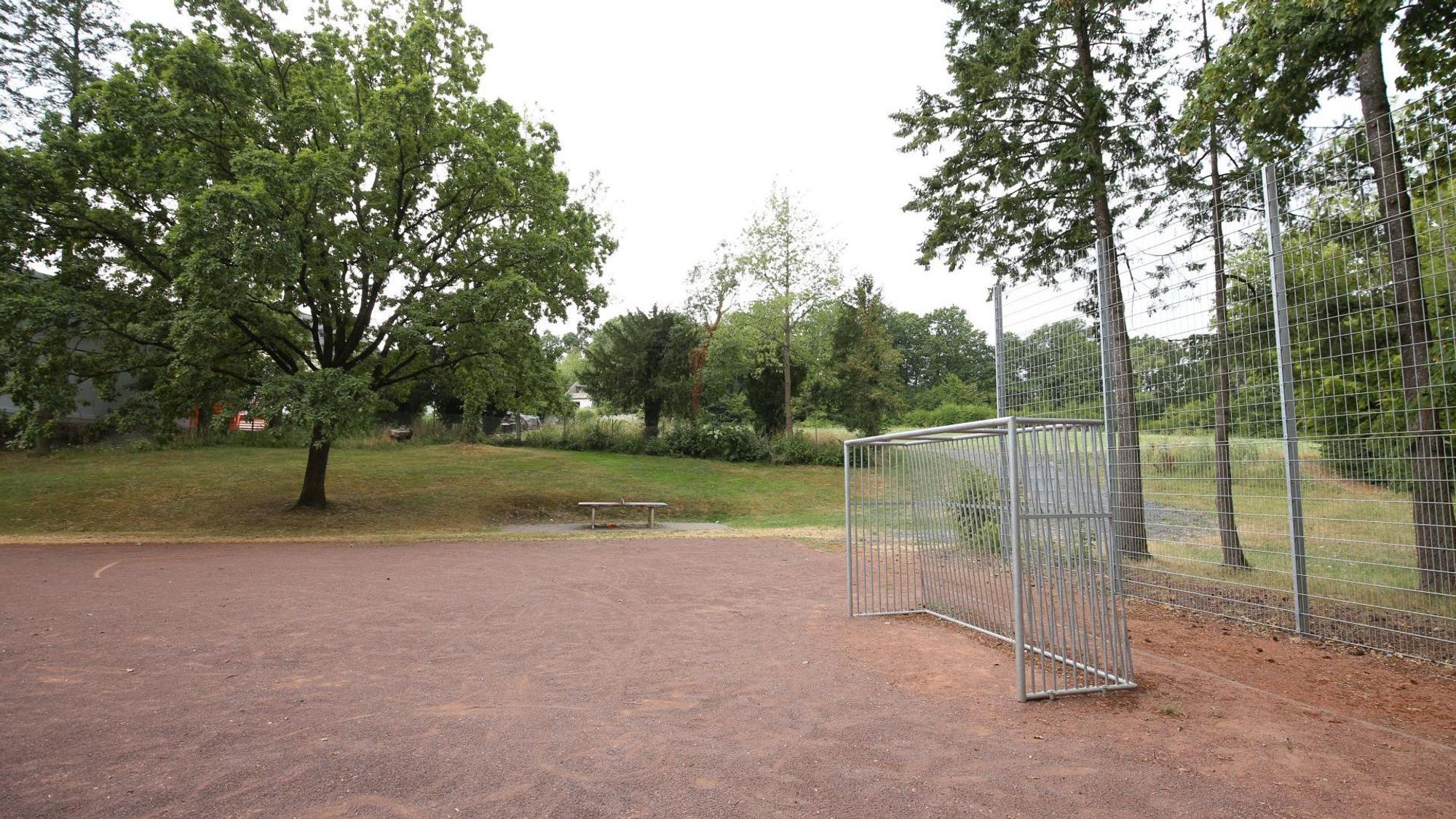 Ein kleiner Bolzplatz mit einem Fußballtor, im Hintergrund Wiesen und Bäume.