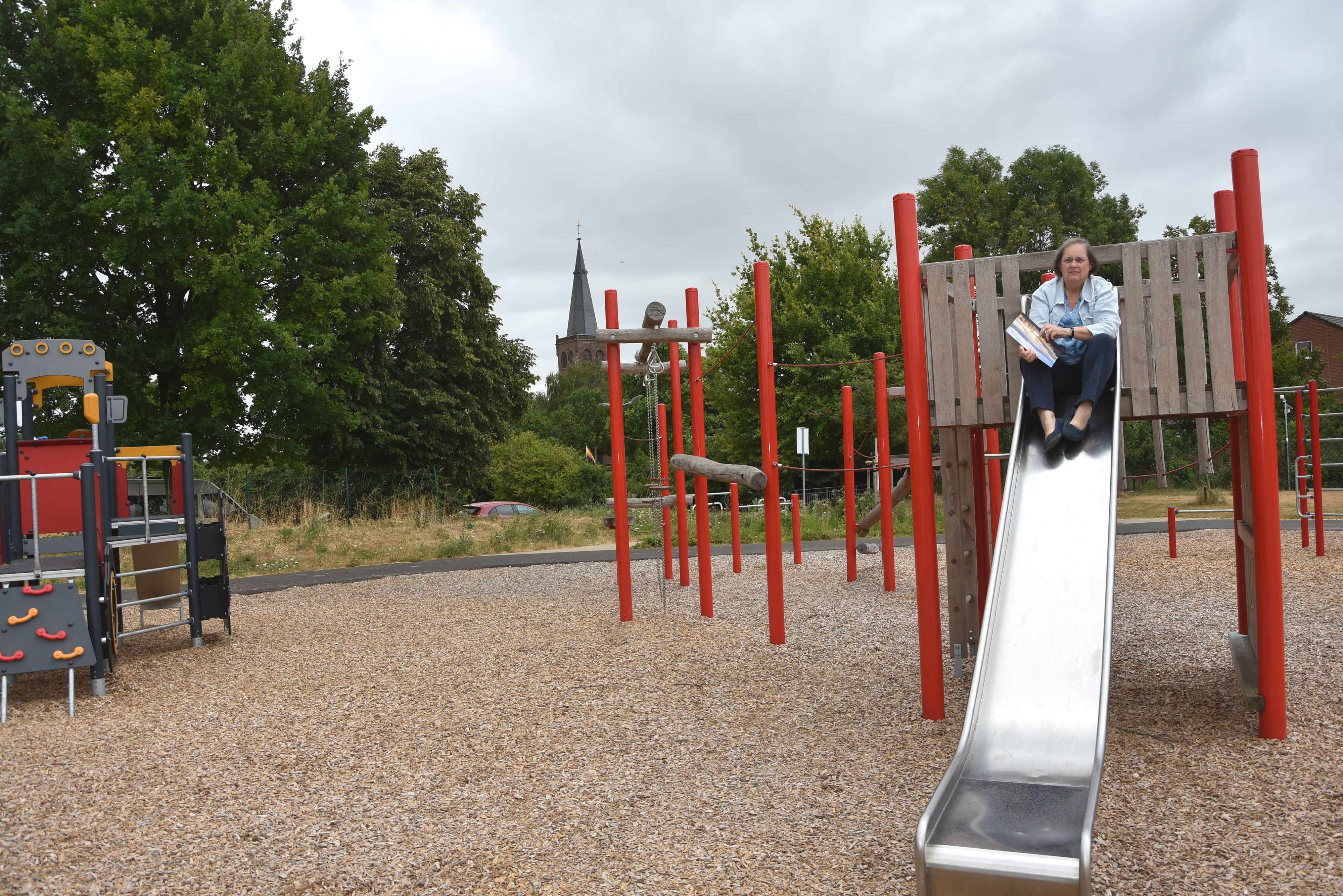 Das Foto zeigt eine Frau, die auf einer Rutsche auf einem Spielplatz sitzt.