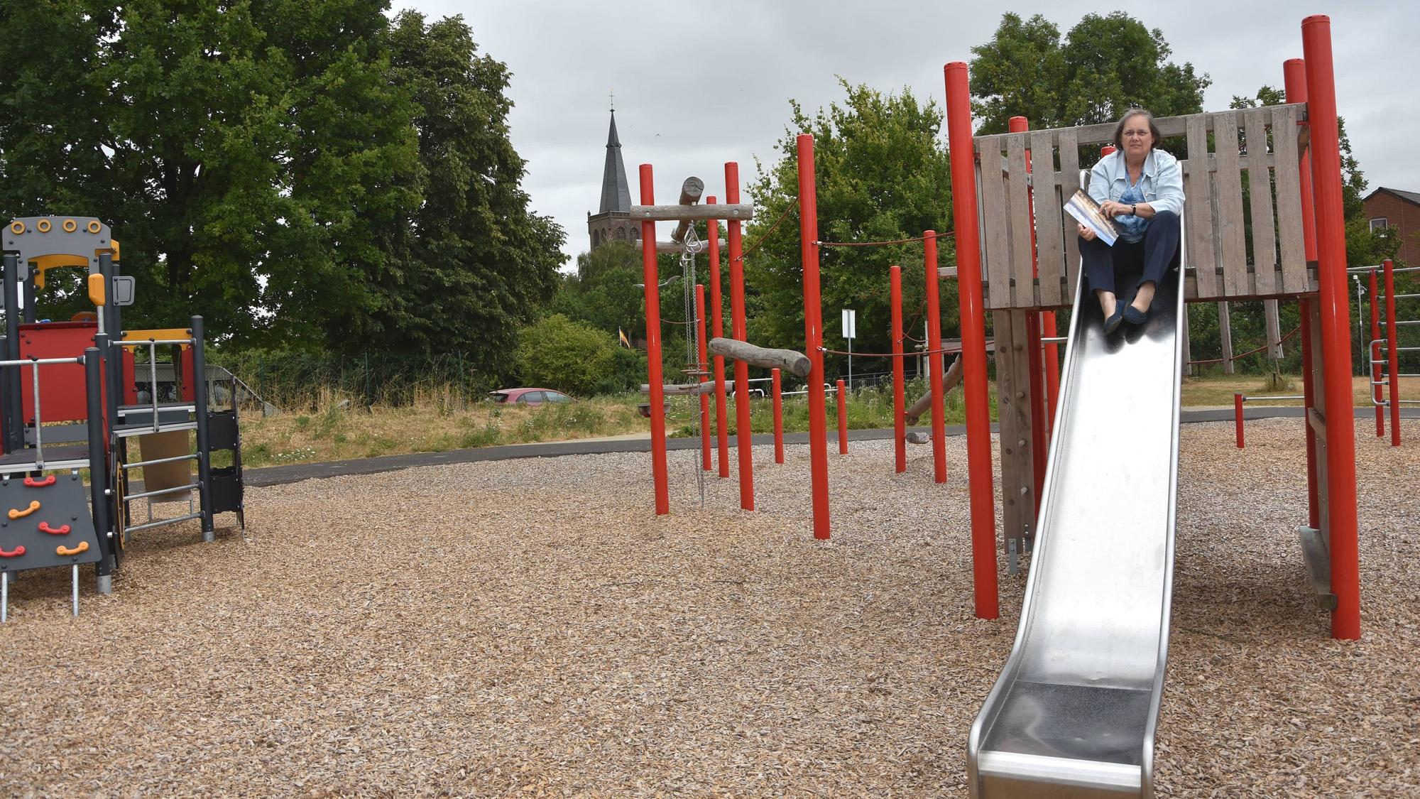 Das Foto zeigt eine Frau, die auf einer Rutsche auf einem Spielplatz sitzt.