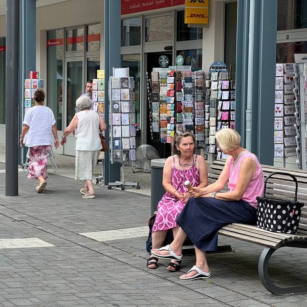 Zwei Frauen sitzen auf einer Bank, sie unterhalten sich.