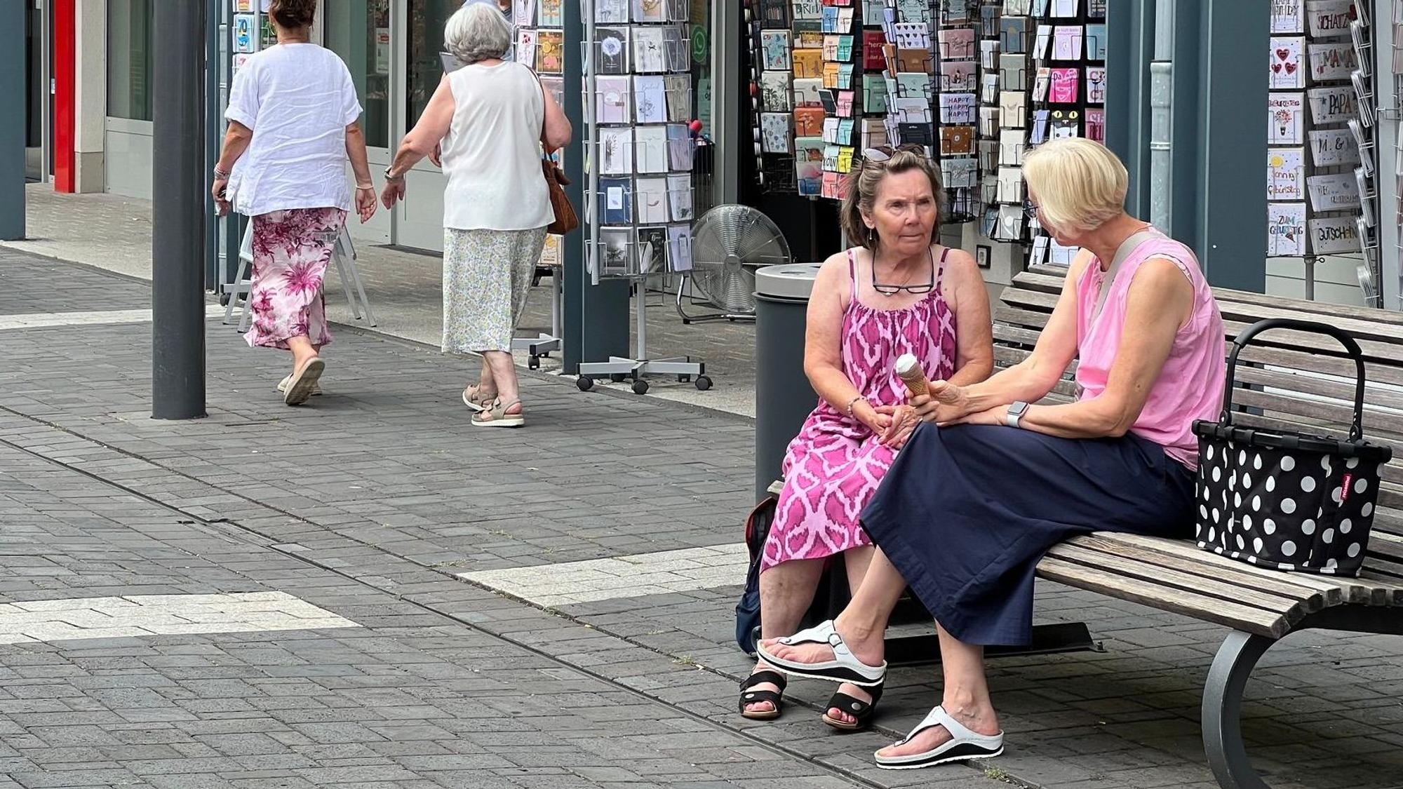 Zwei Frauen sitzen auf einer Bank, sie unterhalten sich.