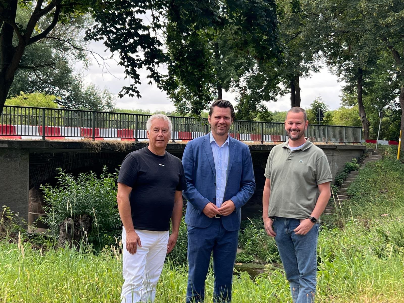 Das Fotos zeigt drei Männer vor einer Brücke.