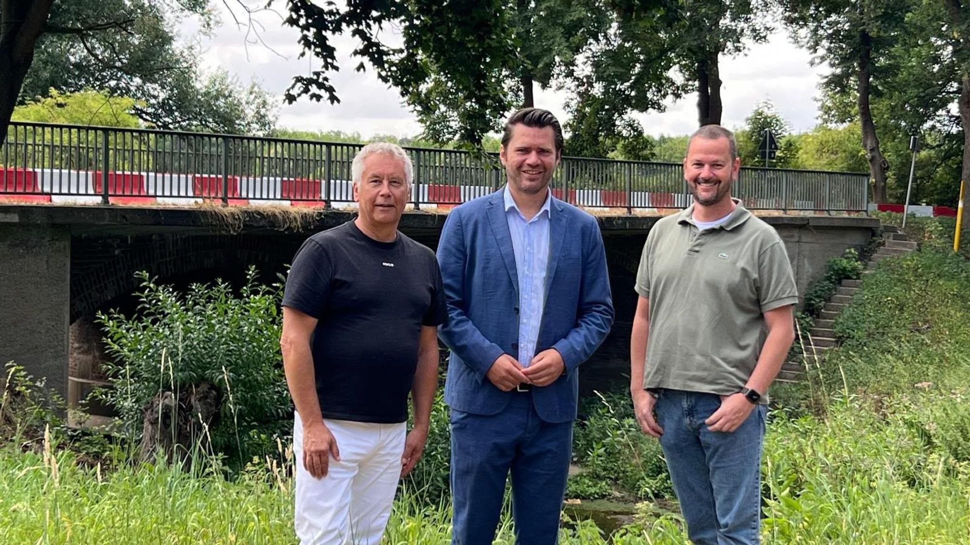 Das Fotos zeigt drei Männer vor einer Brücke.
