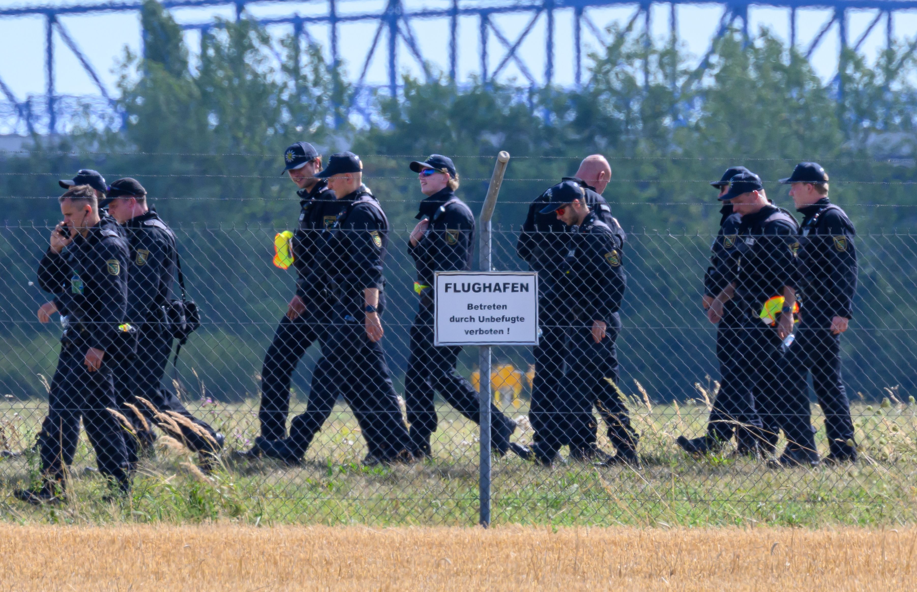 Einsatzkräfte laufen über eine Wiese, davor steht ein Hinweisschild „Flughafen“.