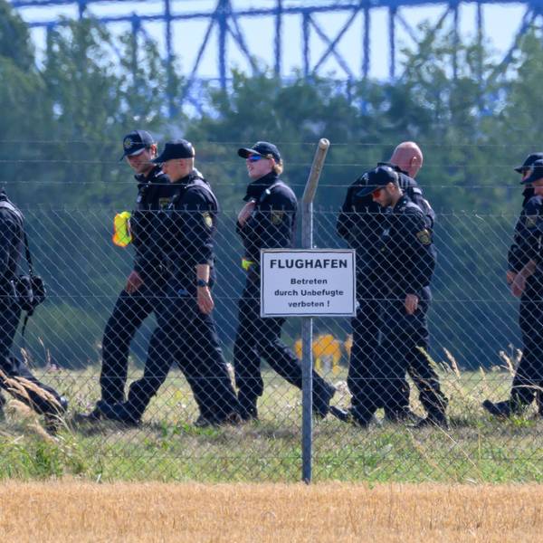 Einsatzkräfte laufen über eine Wiese, davor steht ein Hinweisschild „Flughafen“.