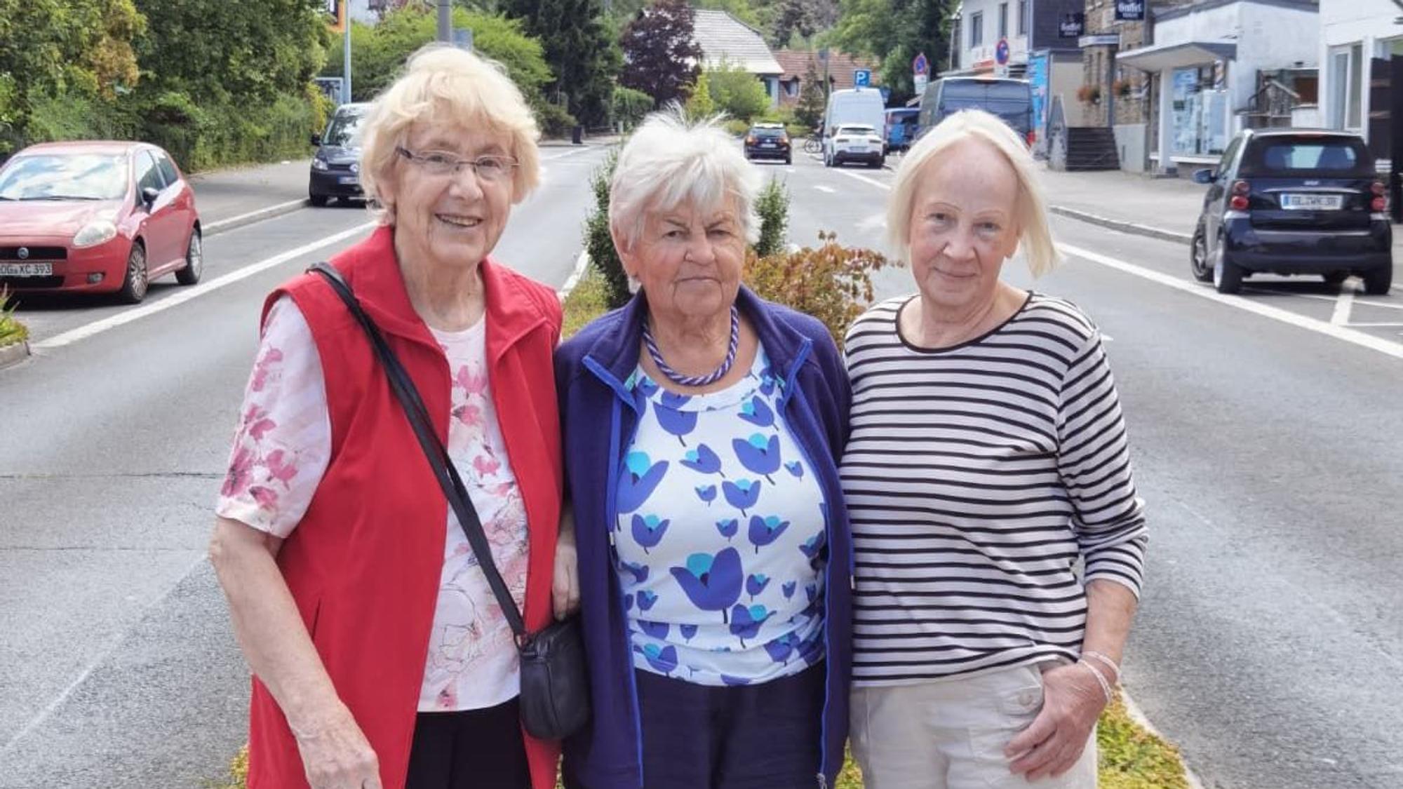 Drei ältere Damen stehen eng nebeneinander und lächeln in die Kamera.