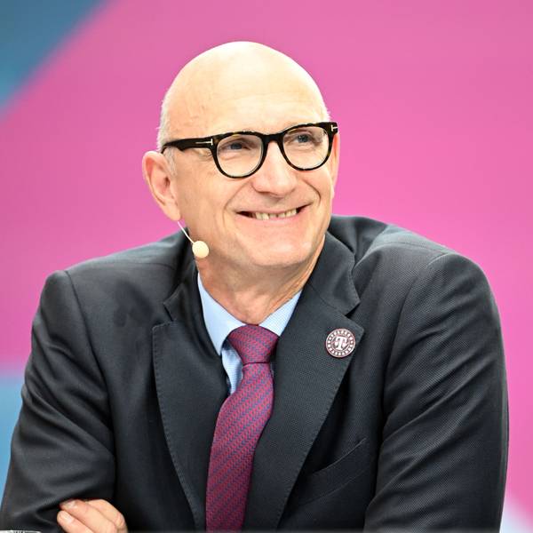 Tim Höttges sitzt vor einem pinken Hintergrund im Anzug und blickt lächelnd an der Kamera vorbei.