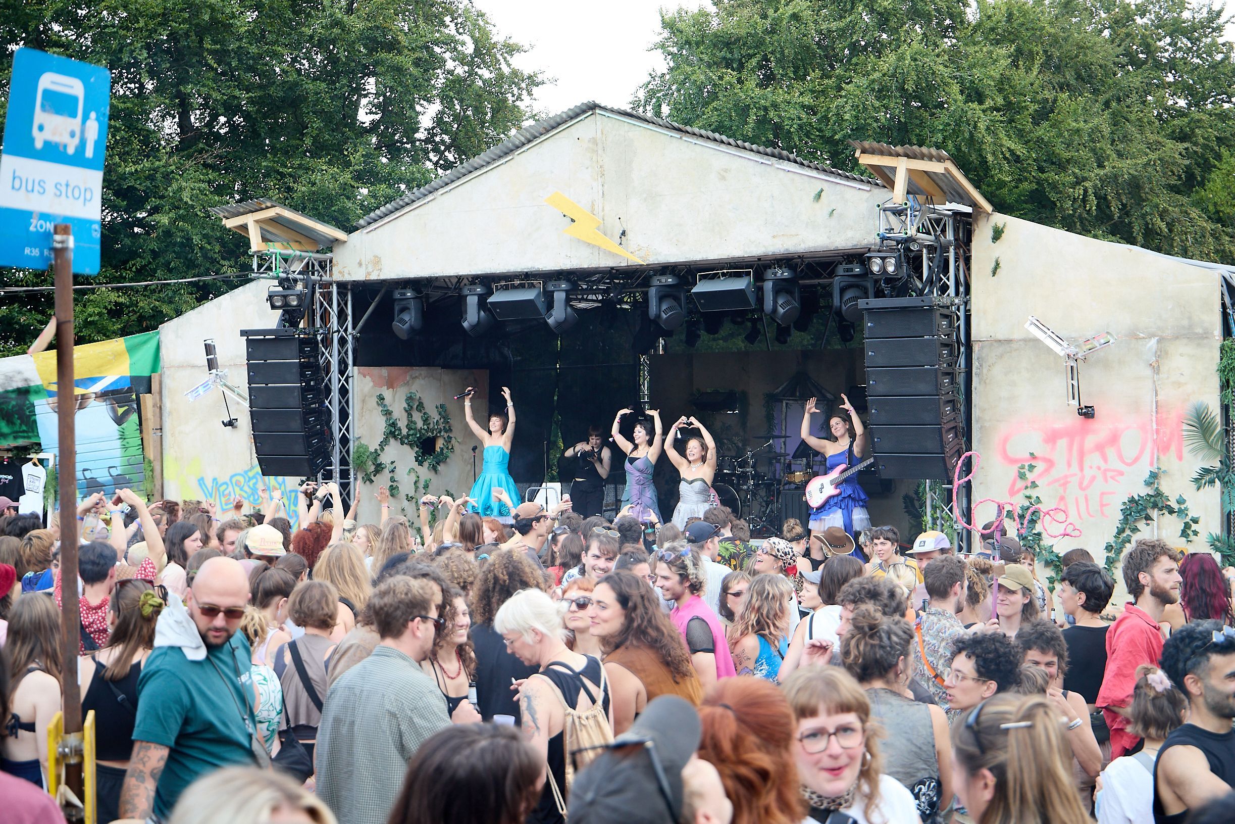 Bandmitglieder heben auf der Bühne des Festivals die Arme, davor stehen die Zuschauer.