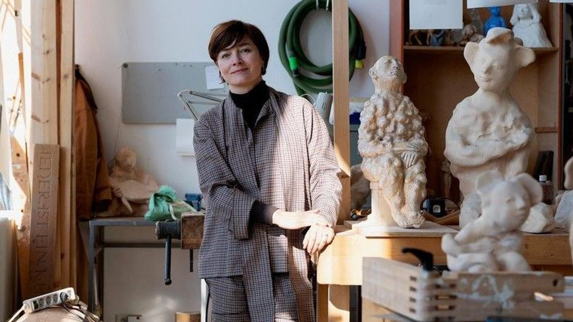 Eine Frau steht in einem Atelier, in Regalen befinden sich mehrere Skulpturen.