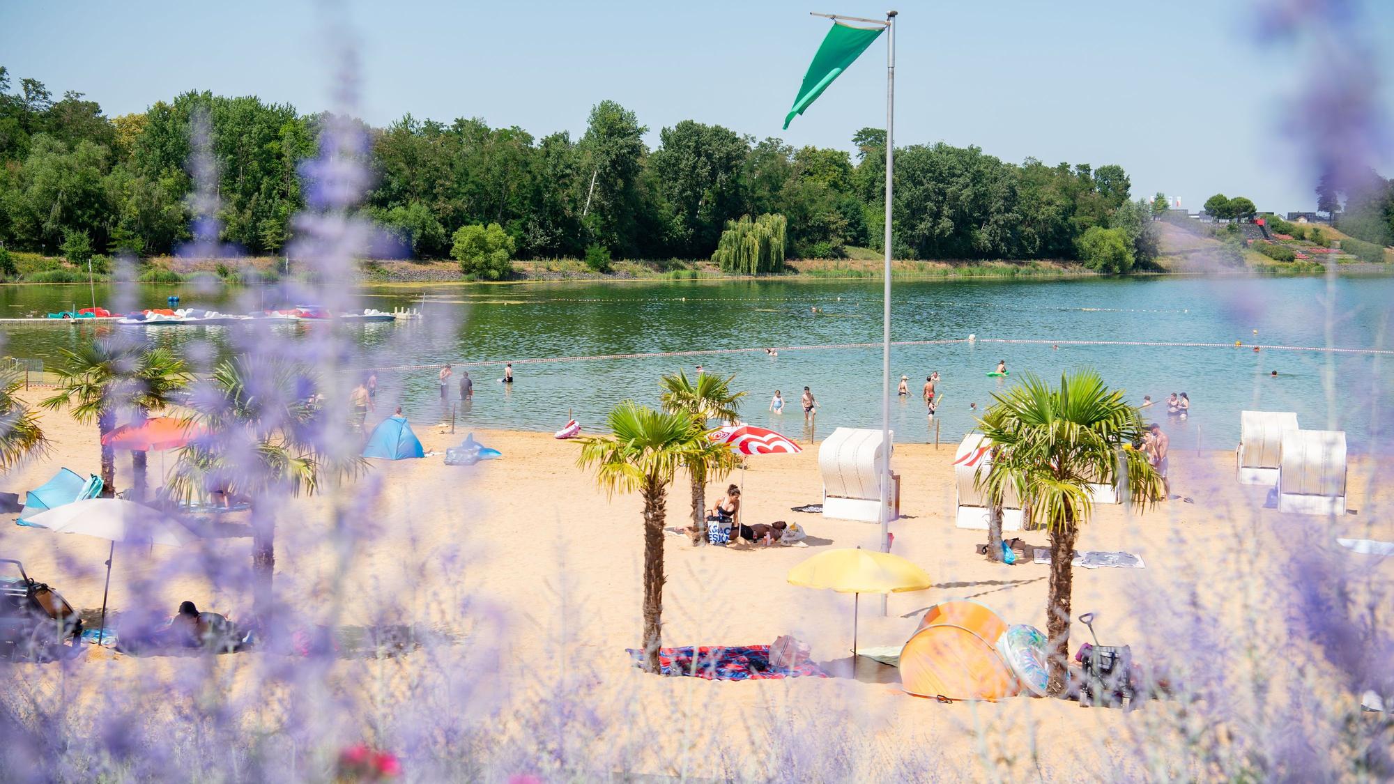 Menschen sitzen unter Palmen am Strand des Zülpicher Badesees.