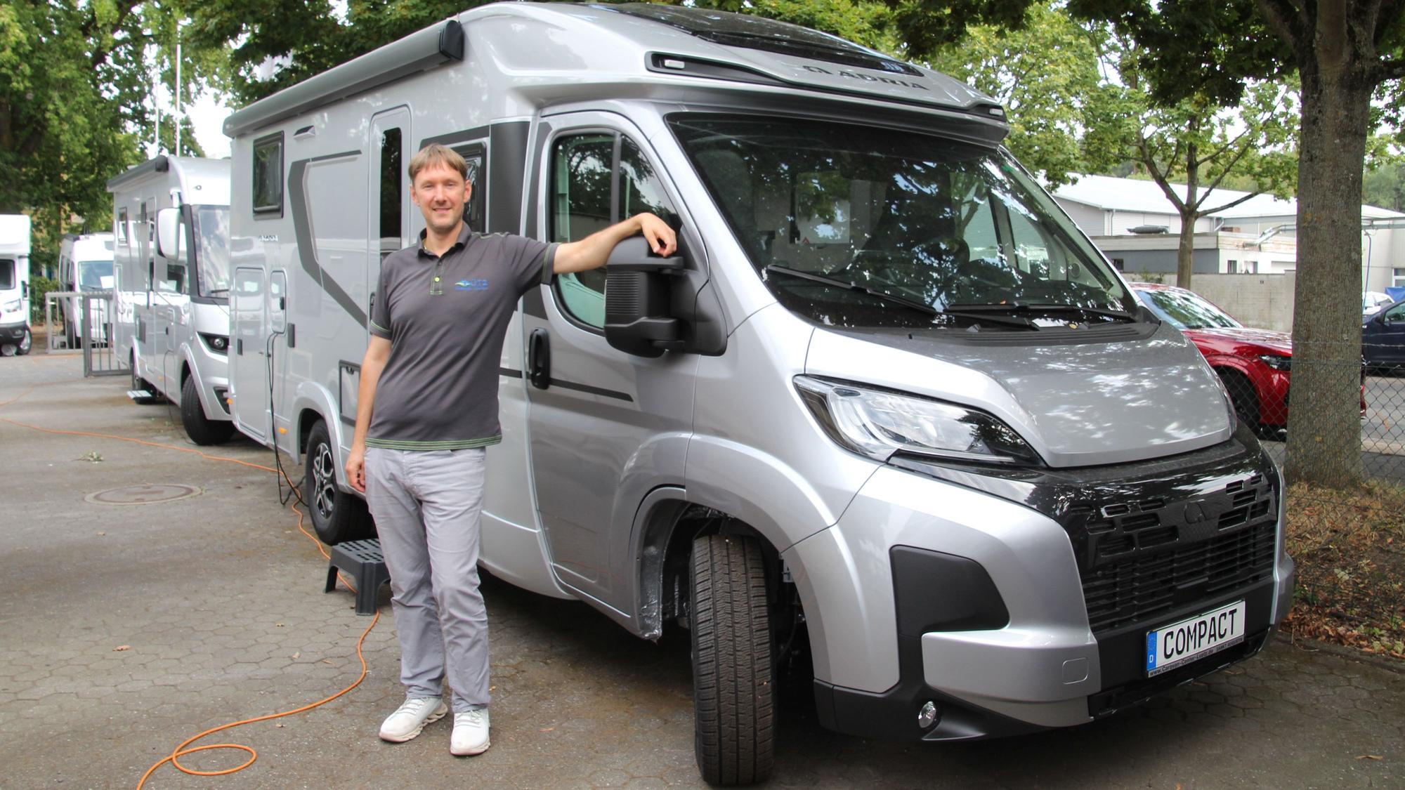 Ein Mann steht vor einem silberfarbenen Wohnmobil.