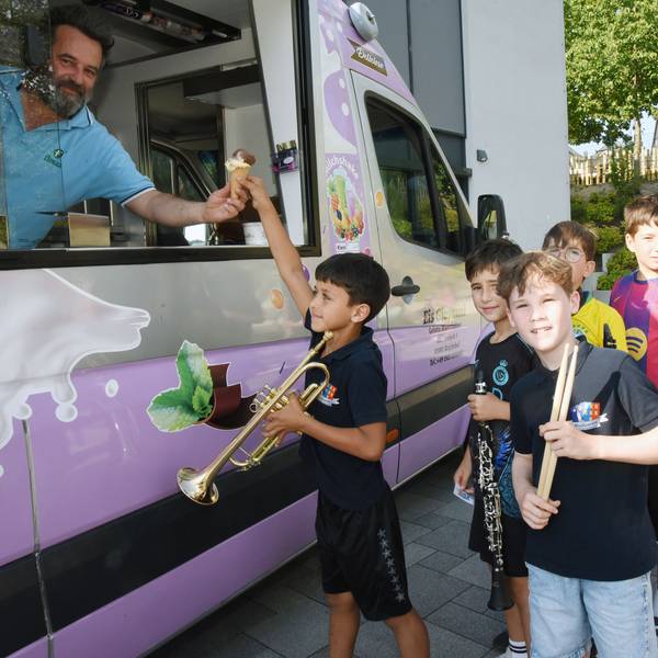 Kinder mit Musikinstrumenten stehen vor einem Eiswagen.