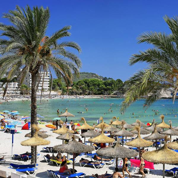 Urlauber an einer Badebucht mit Sonnenschirmen und Palmen.