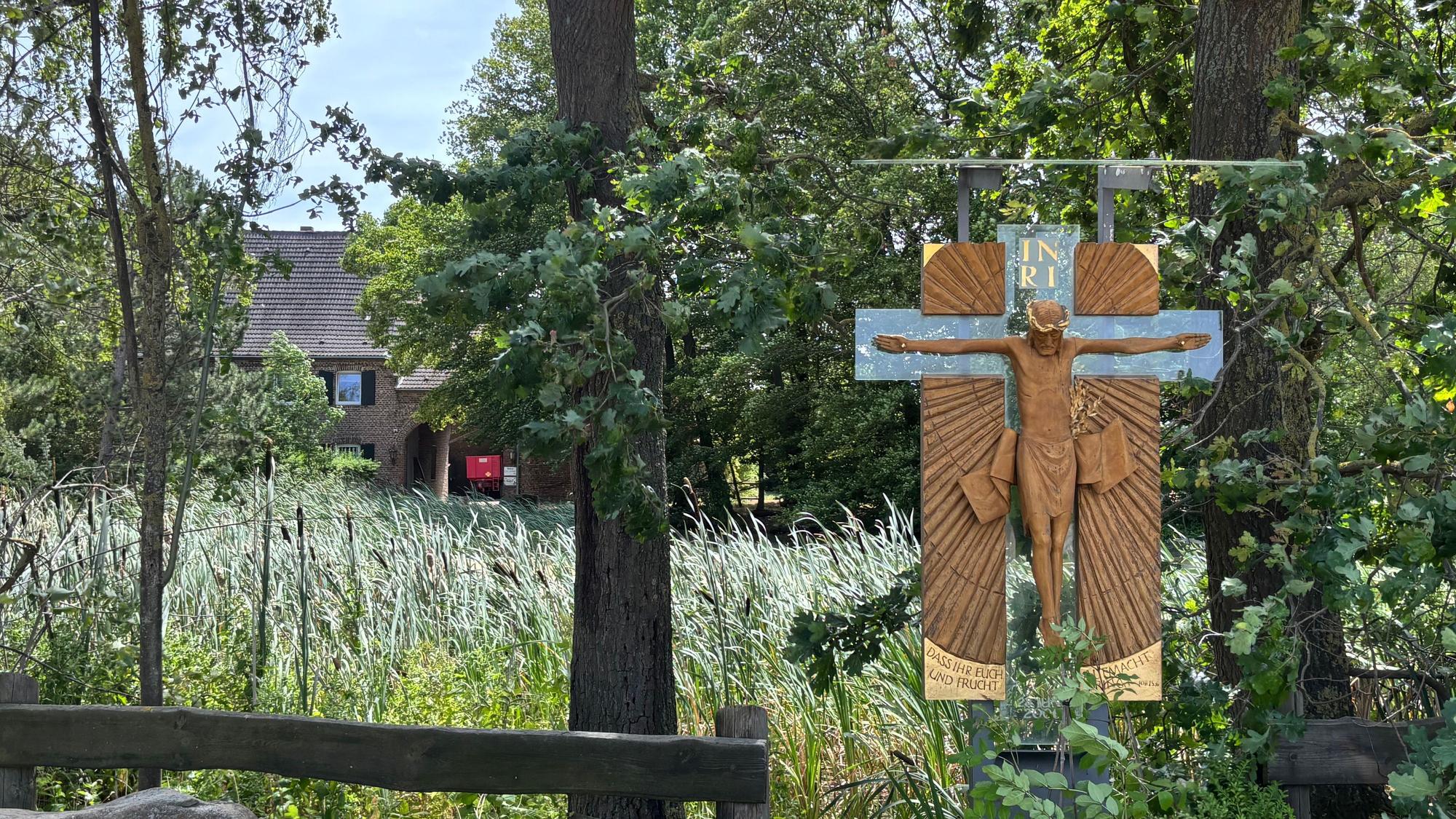 Das Foto zeigt ein Kreuz vor einem Gutshof.