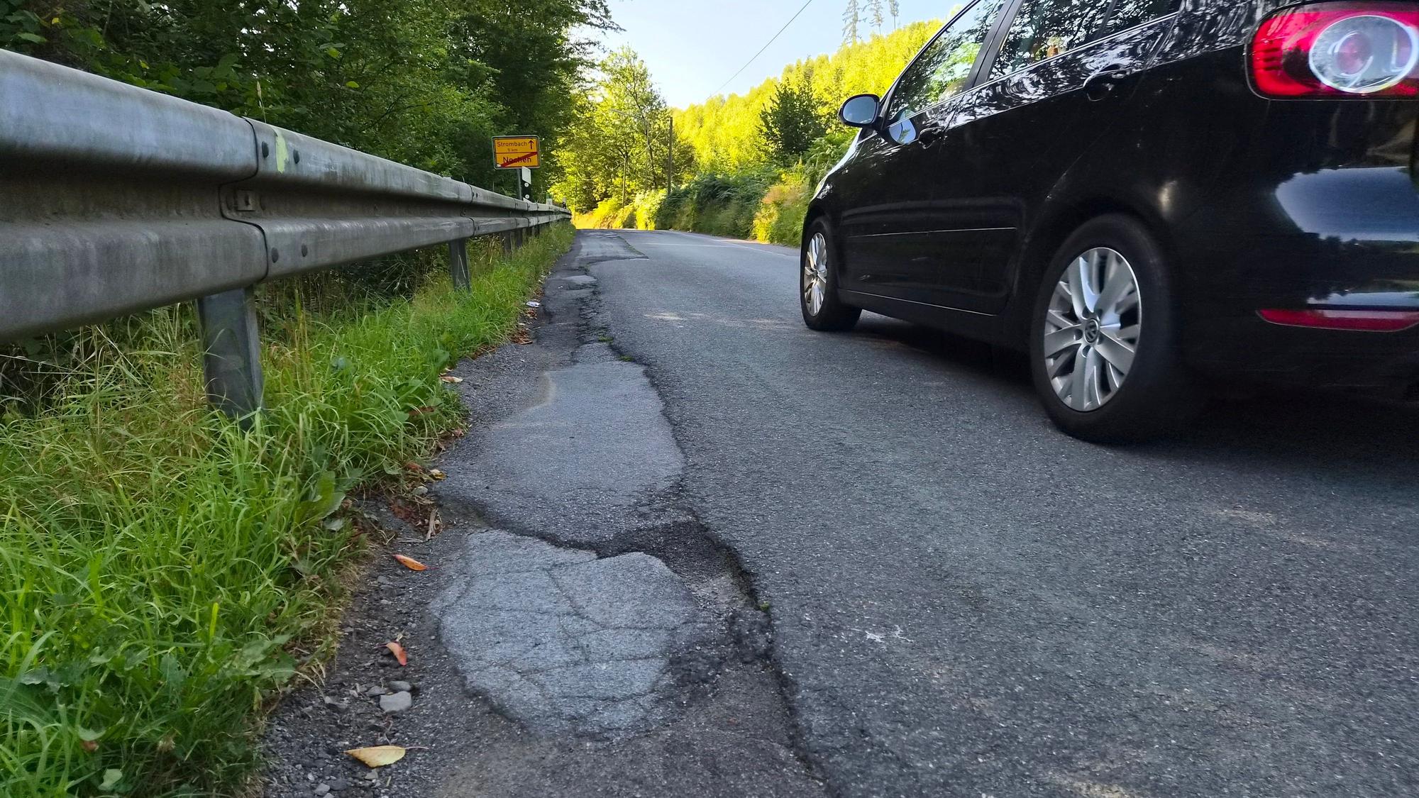 Ein Auto neben kaputtem Asphalt.