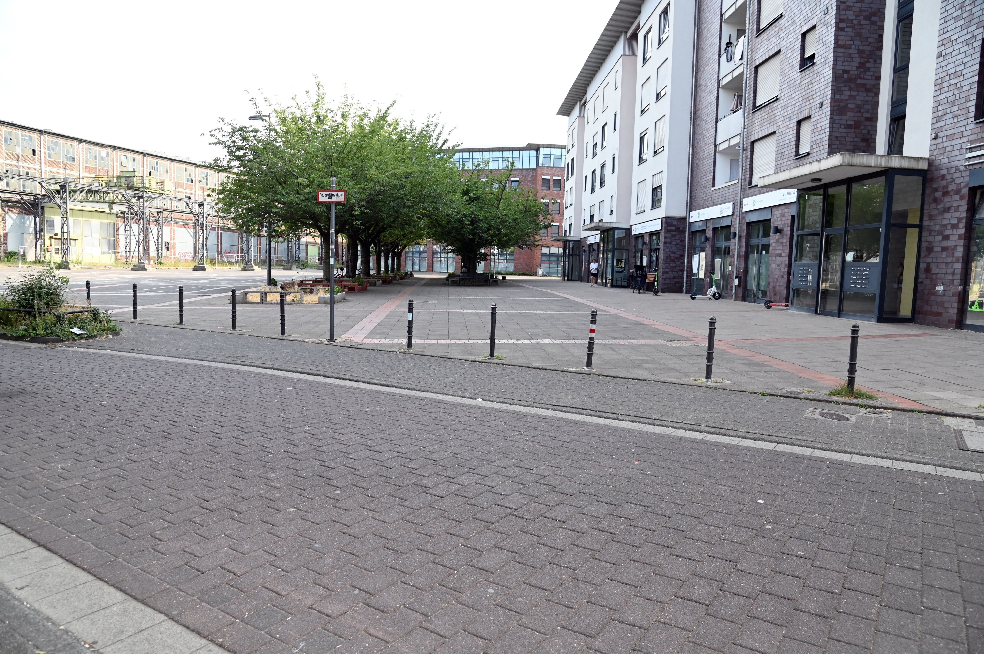 Hinter einer Straße liegt ein Platz, auf der fernen Seite liegen alte Industriehallen.