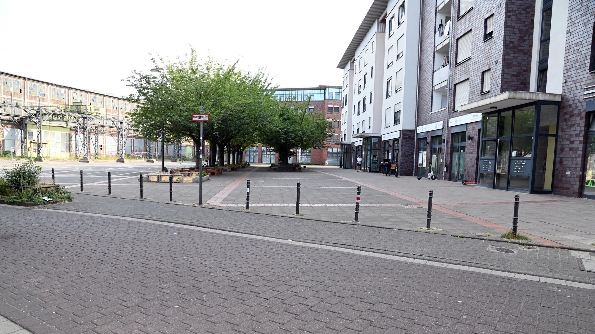 Hinter einer Straße liegt ein Platz, auf der fernen Seite liegen alte Industriehallen.