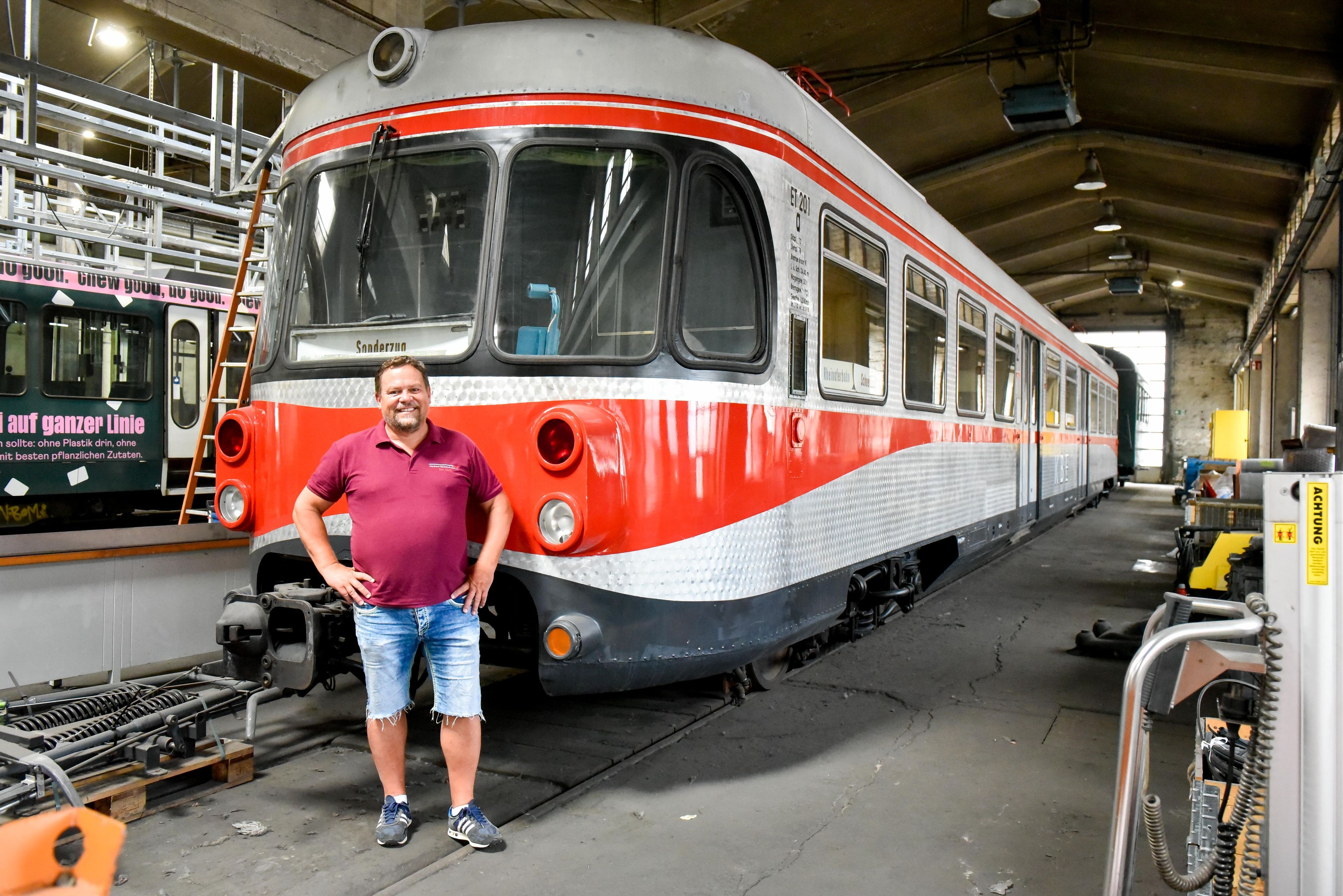 Das Foto zeigt einen Mann, der vor einer alten Bahn steht.