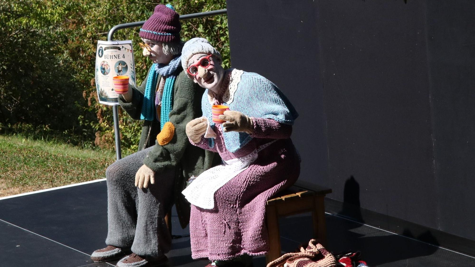 Zwei komplett in Stricksachen gekleidete Darsteller als älterer Mann und ältere Frau.