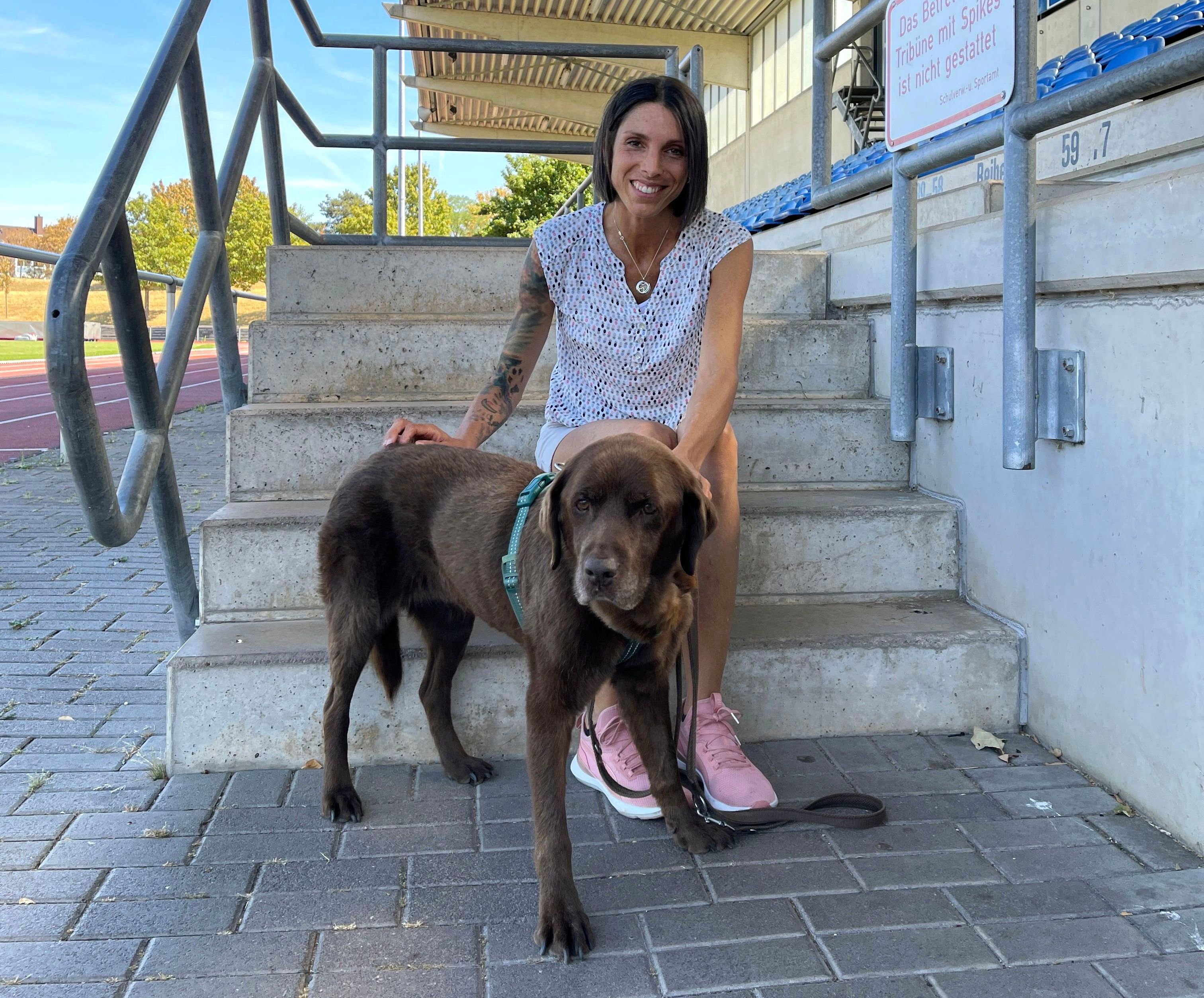 Kristina Marten sitzt auf der Treppe im Heinz-Flohe-Stadion, vor ihr steht einer ihrer Hunde.