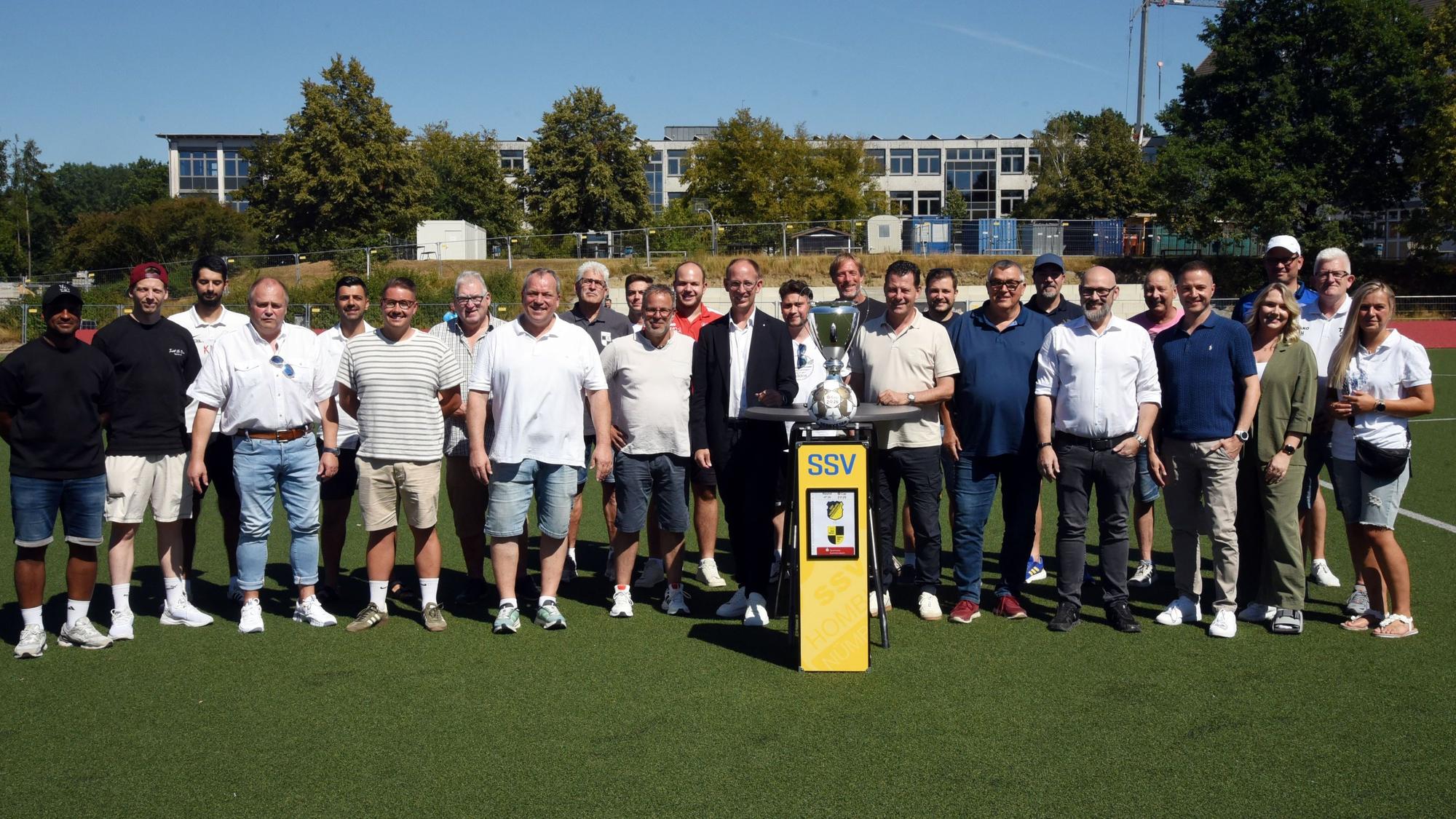 Gruppenfoto aller Verantwortlicher mit dem Pokal in der Mitte.