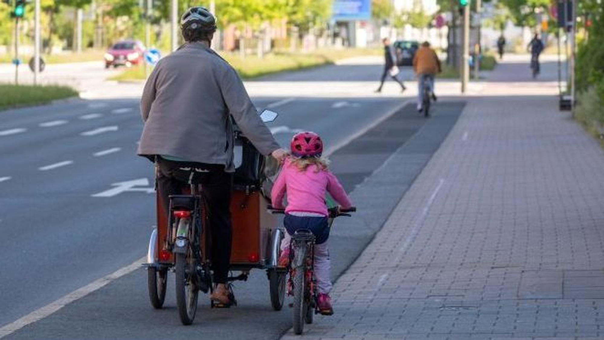 Ein Mann fährt mit einem Lastenrad, daneben fährt ein Kind auf einem Kinderrad.
