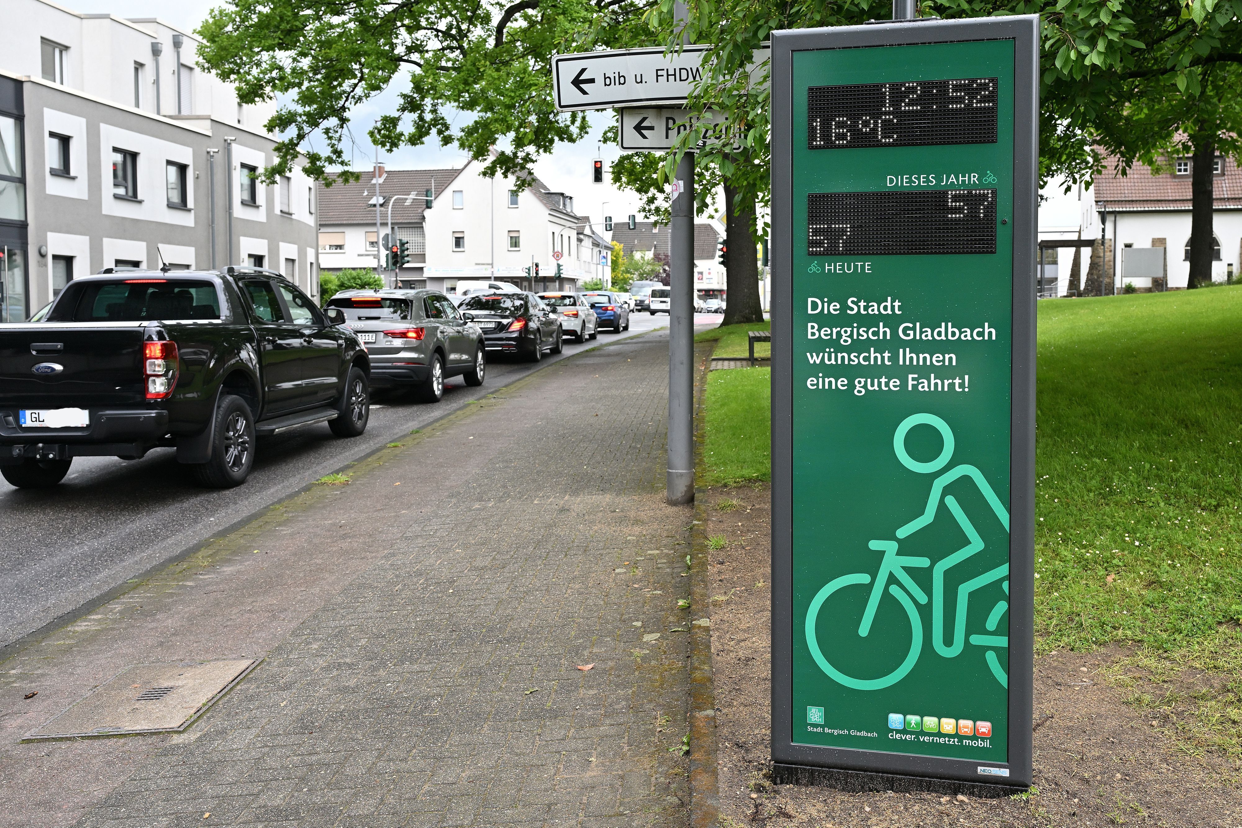 Autos in einer Schlange, daneben eine digitale Infosäule für Radfahrer