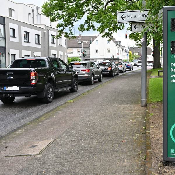 Autos in einer Schlange, daneben eine digitale Infosäule für Radfahrer