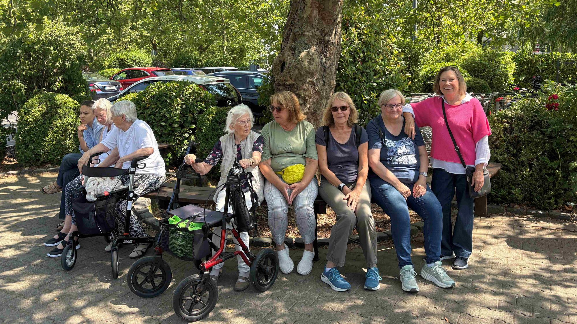 Eine Besuchergruppe sitzt auf einer Bank im Streichelzoo. Manche haben einen Rollator dabei.