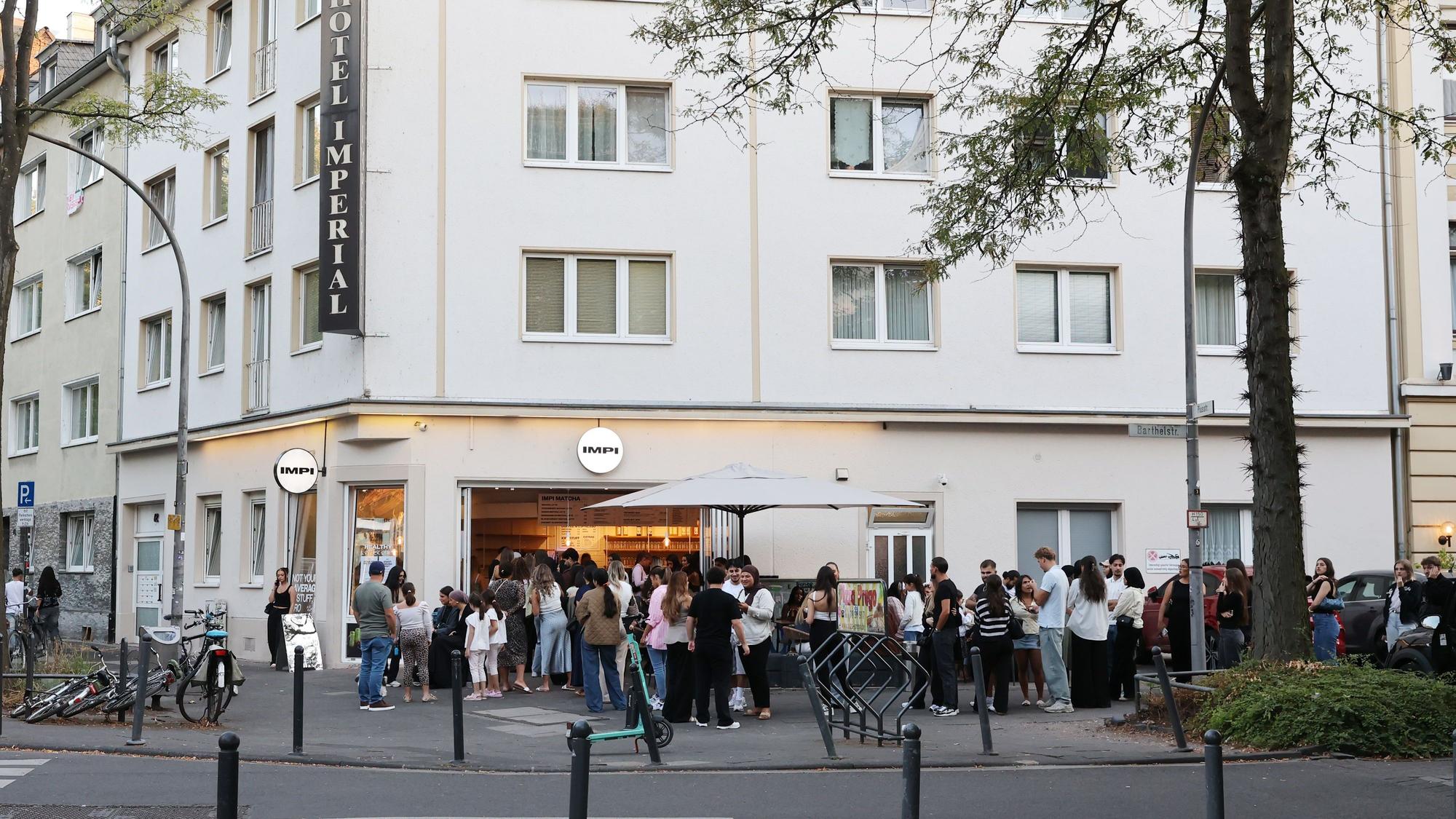 Eine lange Schlange junger Menschen wartet vor einem Eck-Café.