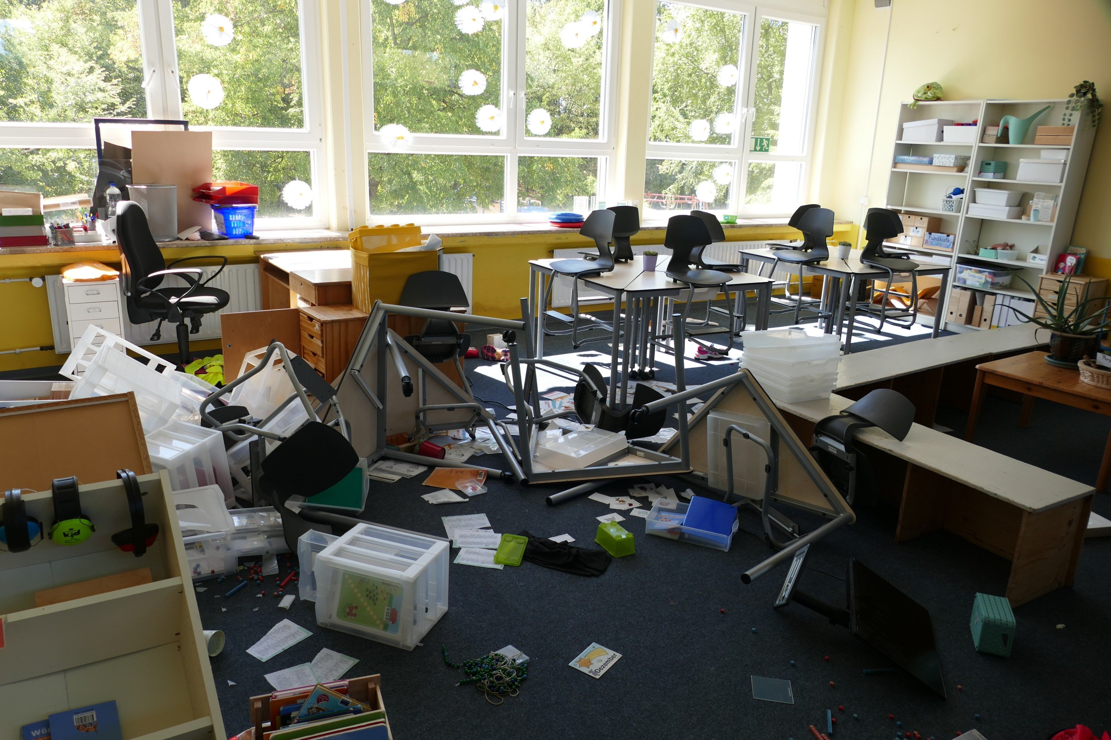 EIn Klassenzimmer in einer Grundschule. Stühle und Tische sind umgeworfen, der Inhalt von Regalen liegt auf dem Bodeni.